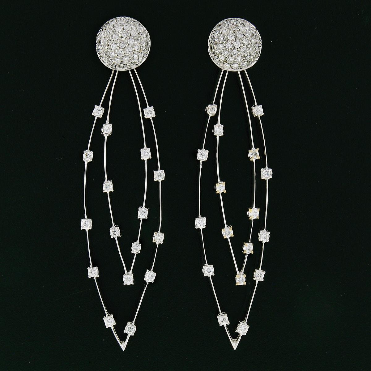 Questo paio di orecchini straordinariamente scintillanti è realizzato in oro bianco massiccio 18 carati e presenta un elegante design lungo con un pezzo pendente che oscilla delicatamente alla base. Gli orecchini sono splendidamente impreziositi da