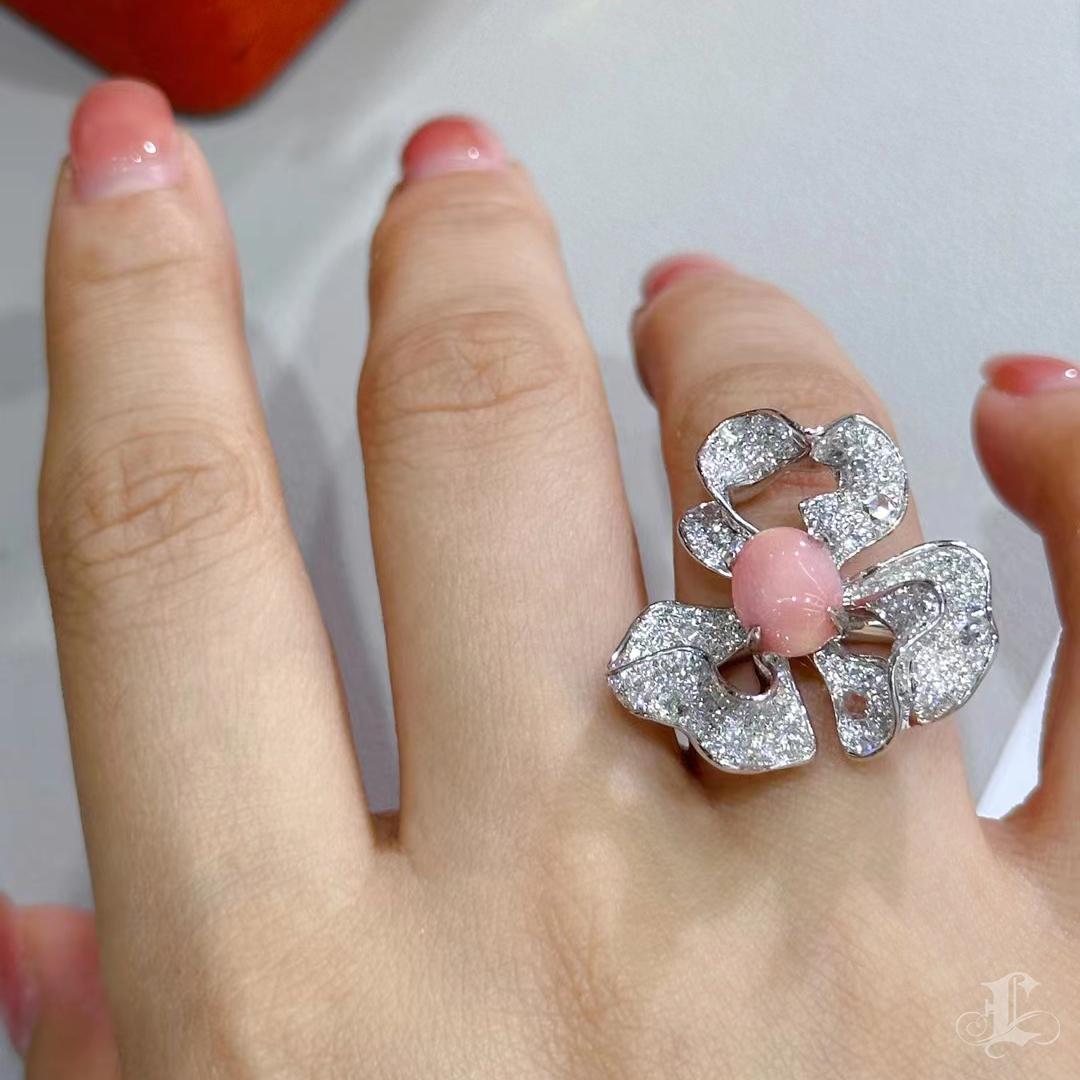 A sculptural daisy unfurls its petals in soft waves, centered around a rare orangey-pink conch pearl weighing 2.63 carats. This symmetrical drop-shaped pearl shows a soft flame and is surrounded by 1.49 carats of SI-quality diamonds in high-polished