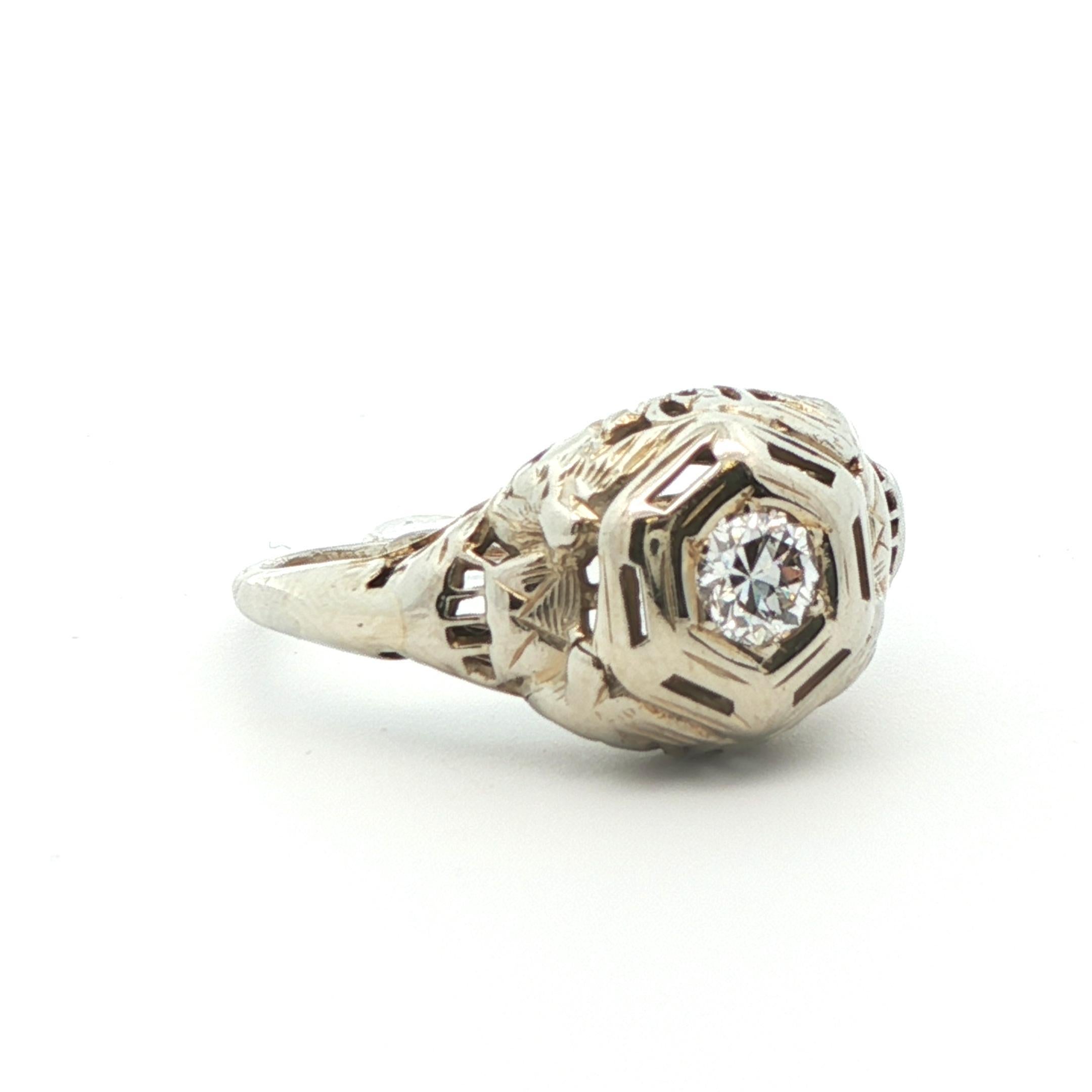 This stunning antique diamond ring comes from the 1925 Art Deco period and was made in 18k white gold. The bright white Old European cut diamond perfectly rests in the center of the ring and is elegantly surrounded with beautiful filigree work. The