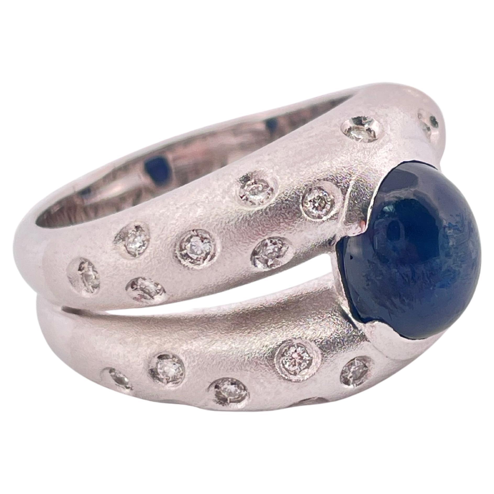 Questo straordinario anello in oro bianco 18 carati presenta un design audace ed elegante, con uno zaffiro cabochon da 2,60 carati al centro. Lo zaffiro blu profondo è incastonato in un castone che ne mette in risalto la superficie liscia e lucente