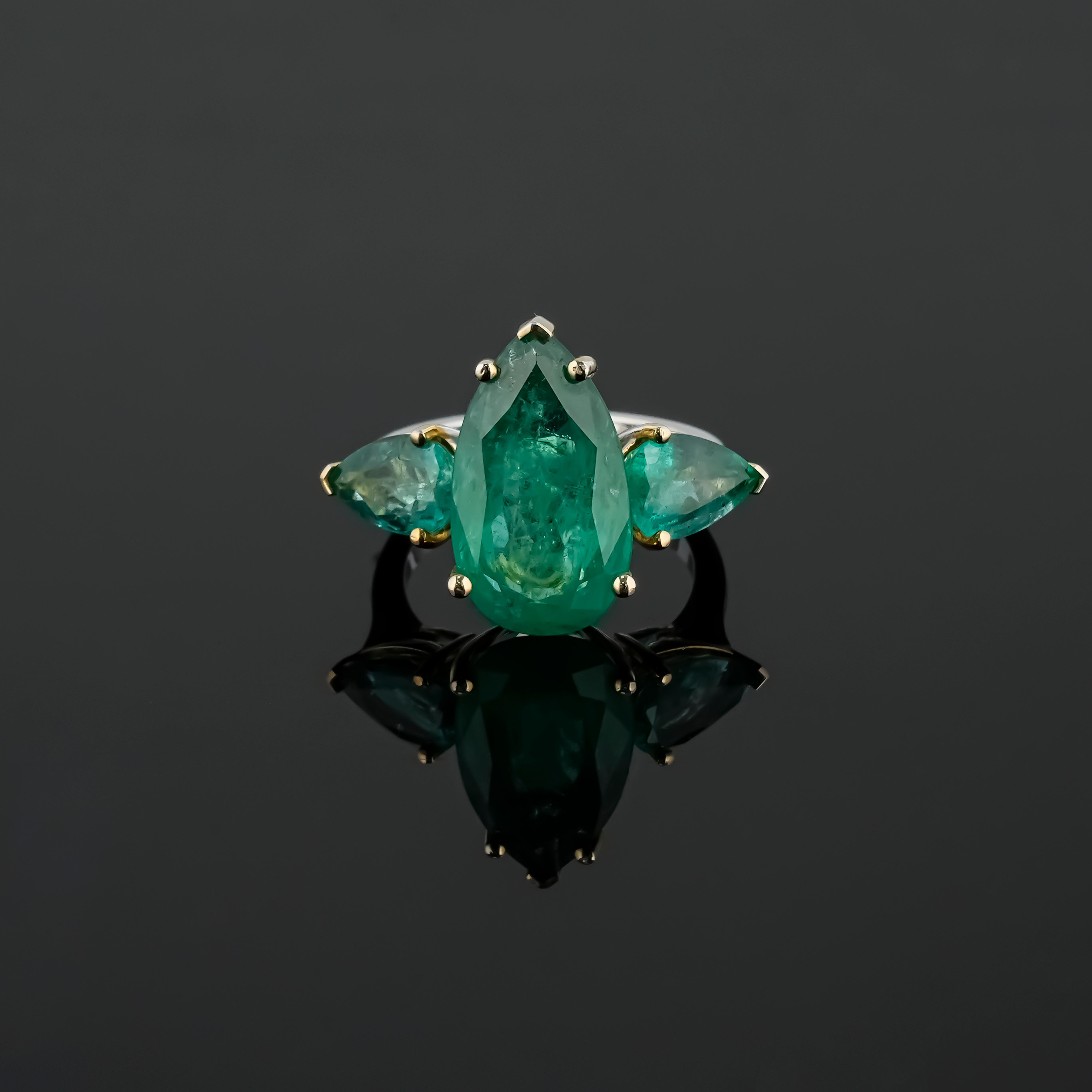 This ring features a 8.26-carat pear-shaped emerald as the central gemstone of Zambian origin, known for its rich green hue. 
It is also flanked by two additional pear-shaped emeralds totaling 2.73 carats, enhancing the overall brilliance and