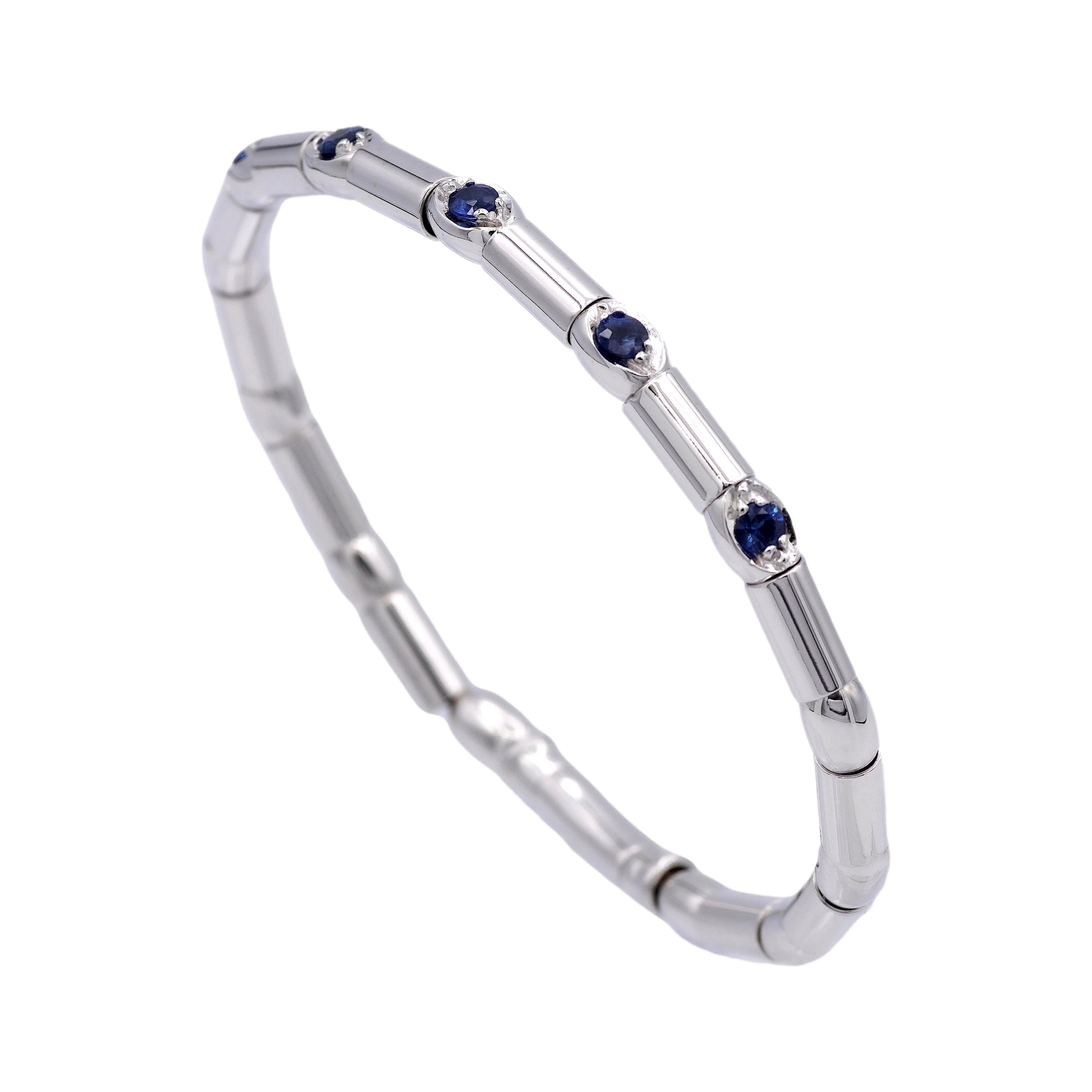 Bracelet finely crafted in 18 karat white gold featuring 5 round brilliant cut blue sapphire sections across the top weighing a total of approximately 0.50 carats set in prongs in a bamboo style with a push down hinge closure mechanism. Metal has