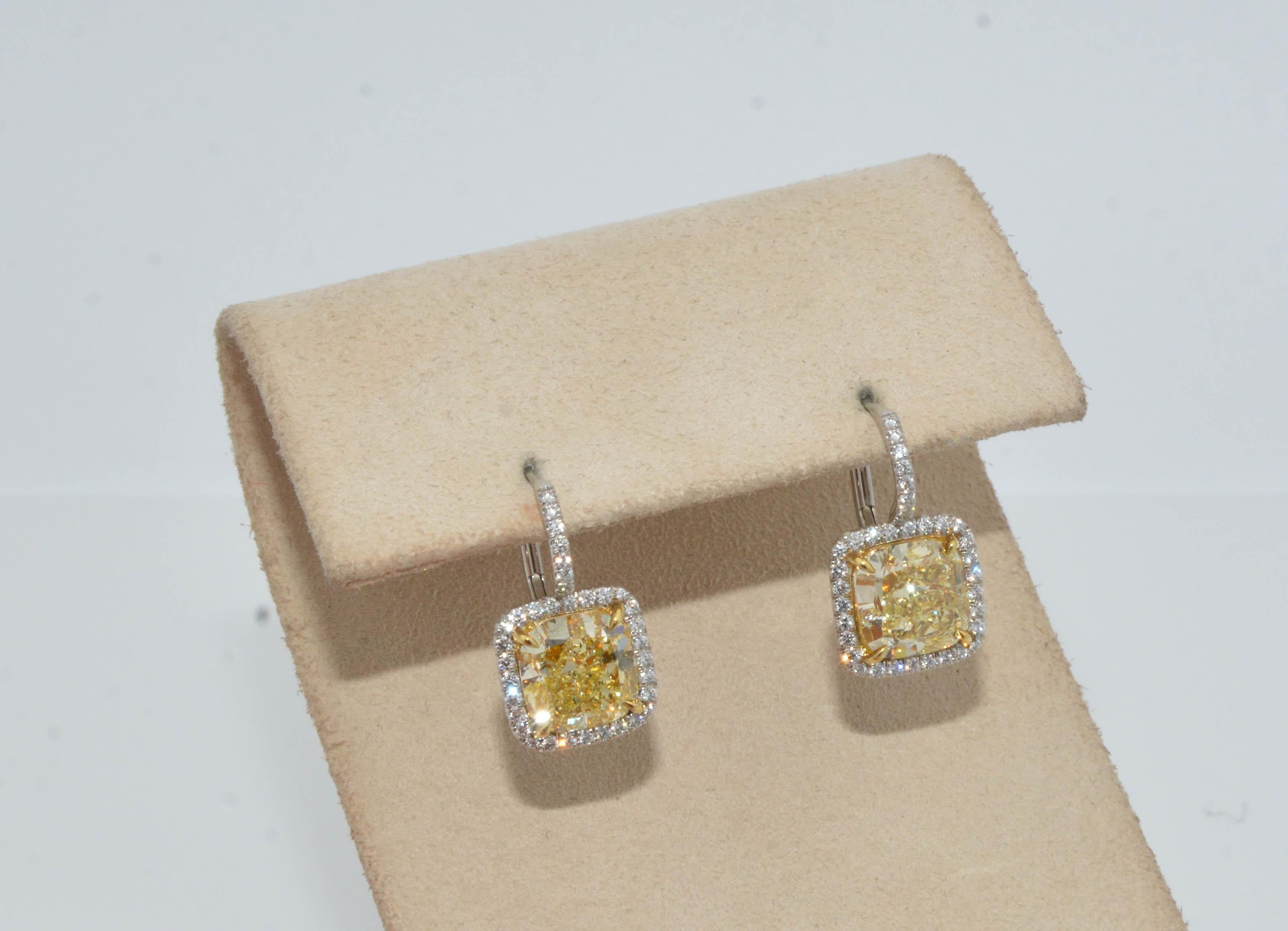 Shine your light all night with these spectacular yellow diamond earrings! Set in 18K white gold with two fancy yellow cushion cut diamonds ( one diamond weighs 2.52ctw and the other weighs 2.58ctw; clarity VVS1). Framing the yellow diamonds is a