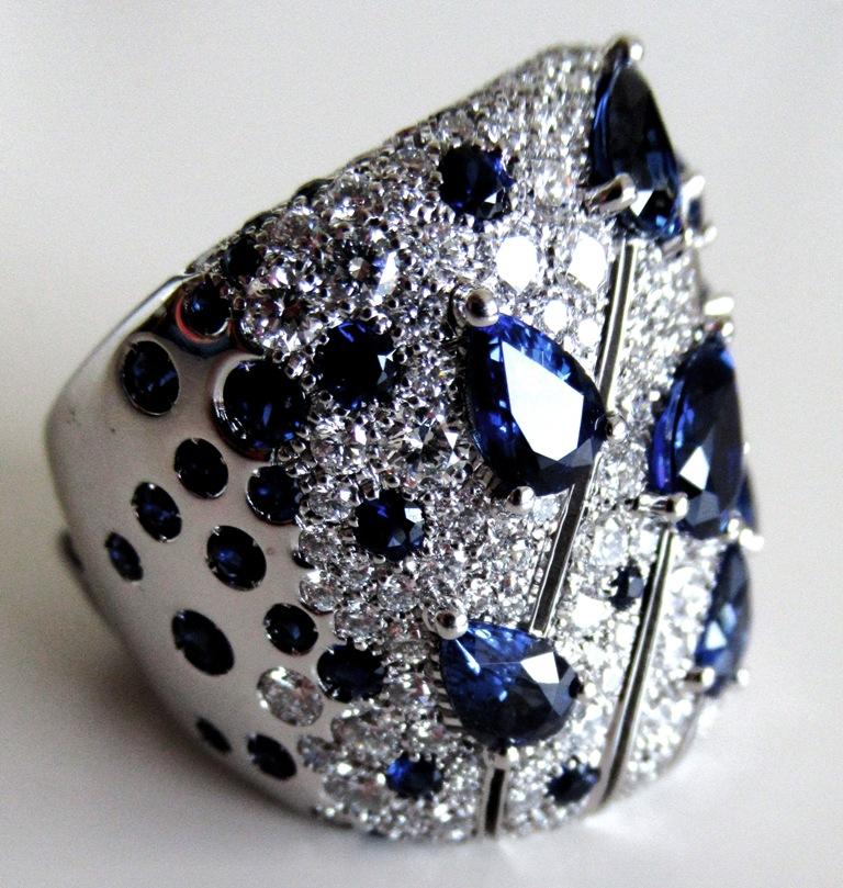 Dramatic 18K white gold wide  band ring with white diamonds pave' and pear shaped blue sapphires. The Unique design is enhanced from the movement created on the top of the ring alternating blue sapphires drops and the white diamonds pave'. 
18K
