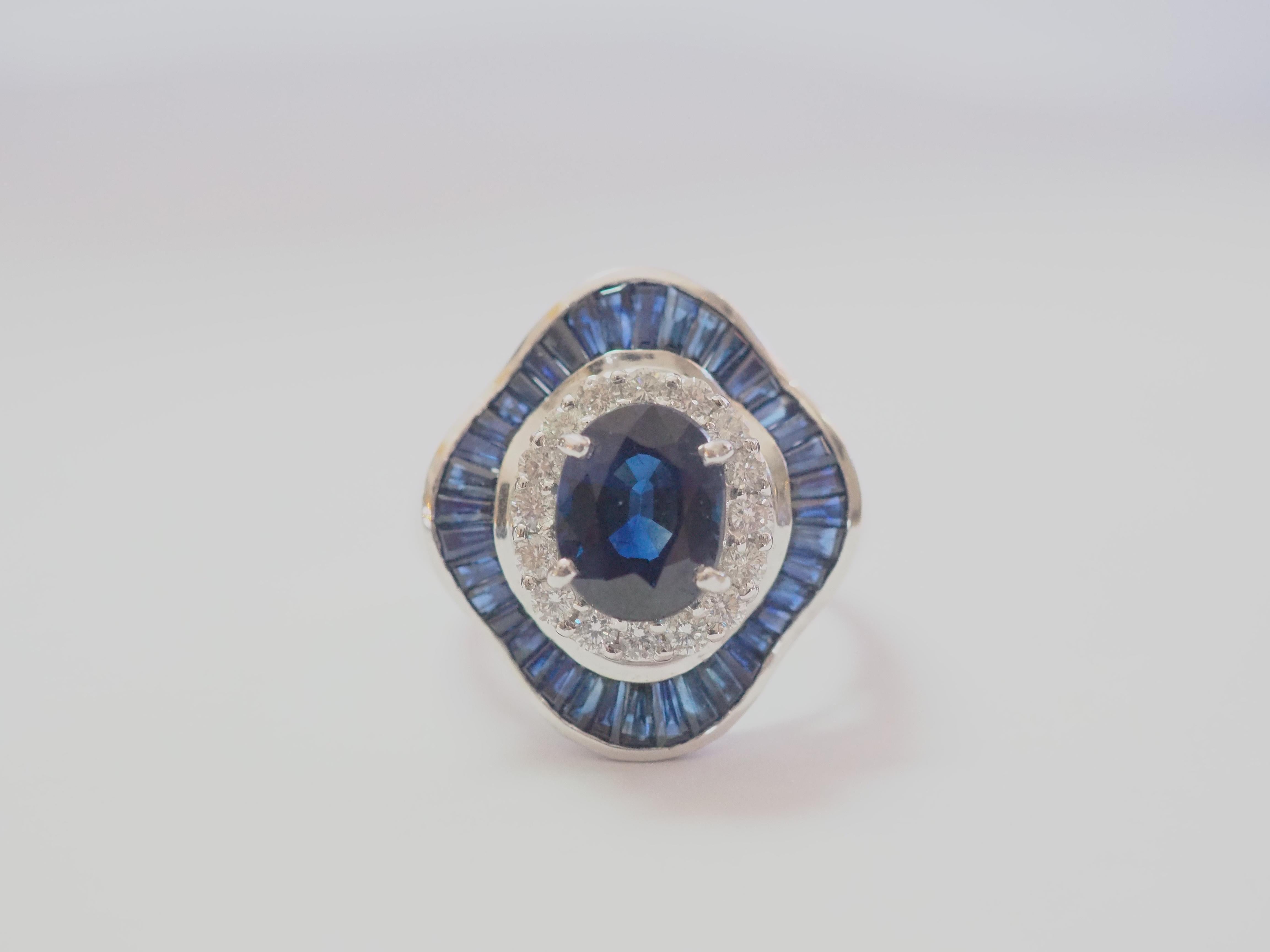 A stunning dark tone Thai royal blue sapphire ring. The oval blue sapphire has a good saturation of blue and with no visible eye inclusions. The diamonds here are brilliant and of very good quality, clear and colorless. The surrounding caliber-cut