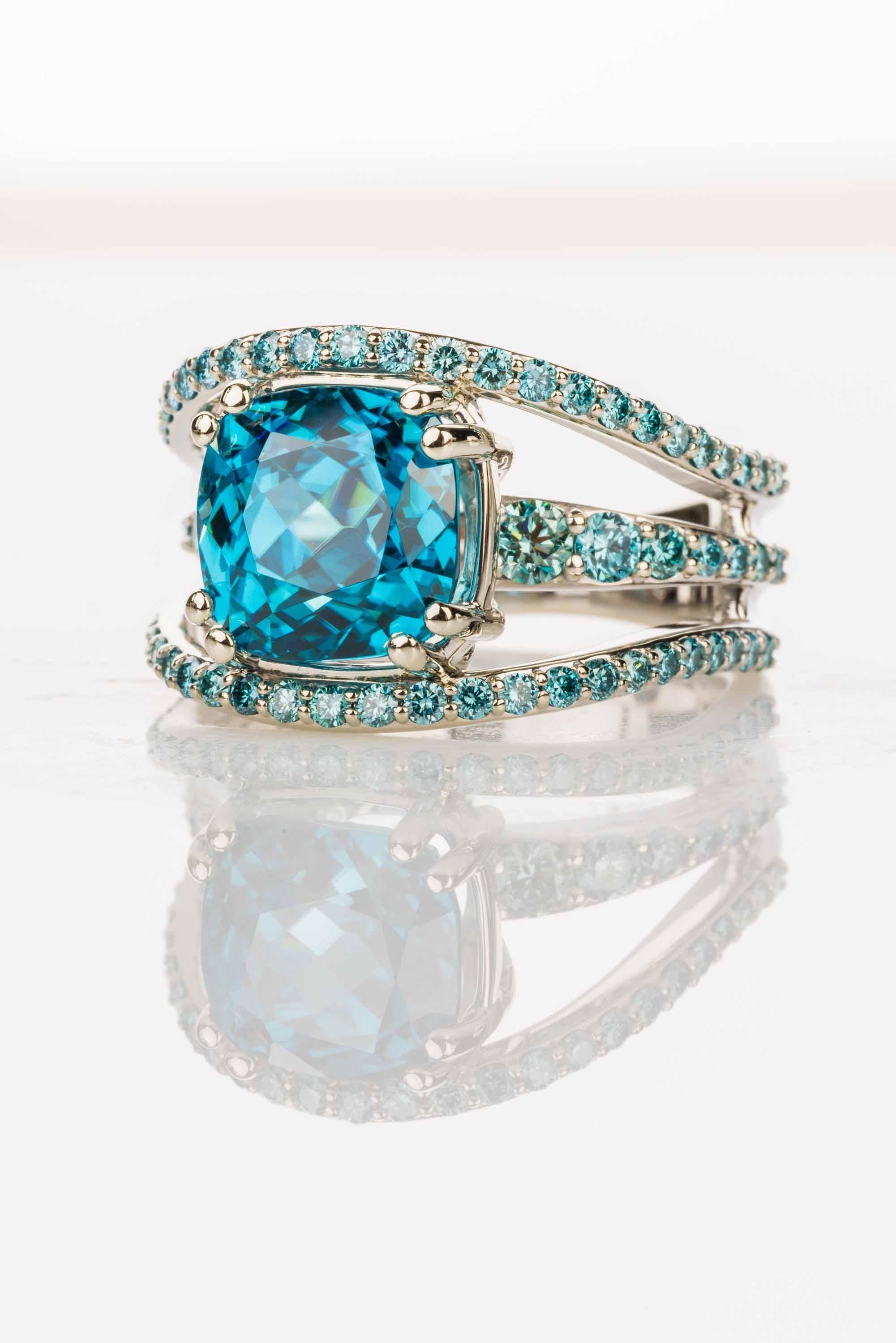 An 18k white gold ring set with a 7.65 carat cushion cut blue zircon and 1.2 total carat weight bead set round blue diamonds, ring size 7. This ring was designed and made by llyn strong.