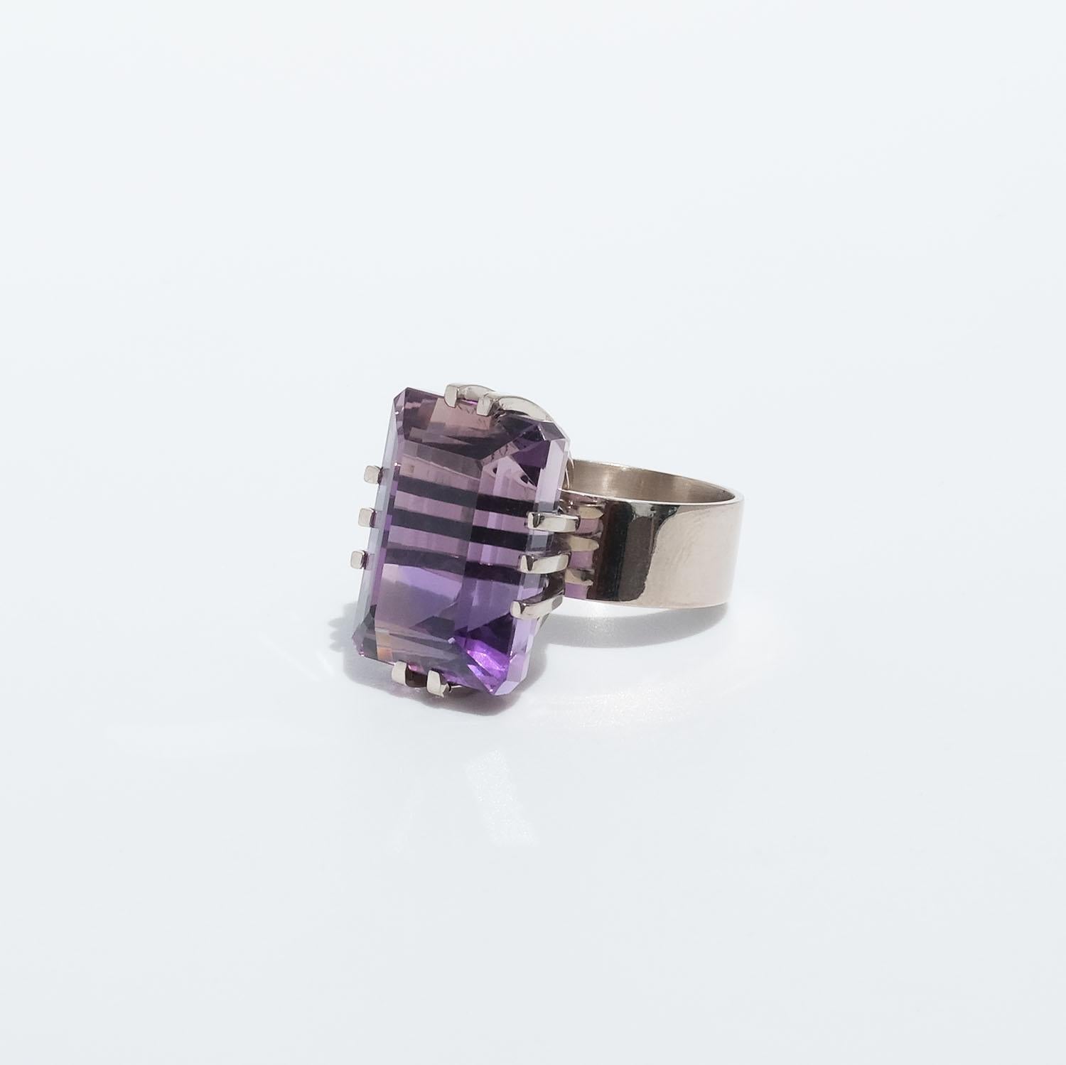 This 18 karat white gold ring is adorned with a rectangular, faceted amethyst that has a deep purple tone. The ten prongs holding the amethyst are prominent and the shank of the ring is beautifully wide and creates a strength in the appearance of