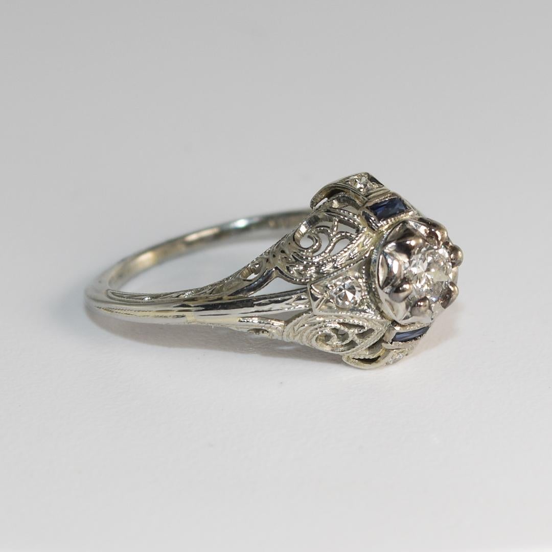Dieser schöne, antike Ring aus 18 Karat Weißgold wiegt 2,40 Gramm.
Er enthält vier kleine runde Diamanten auf jeder Seite mit einem Karatgewicht von 0,02 und einen 3 mm großen runden Brillanten in der Mitte mit einem Karatgewicht von 0,10 und einer