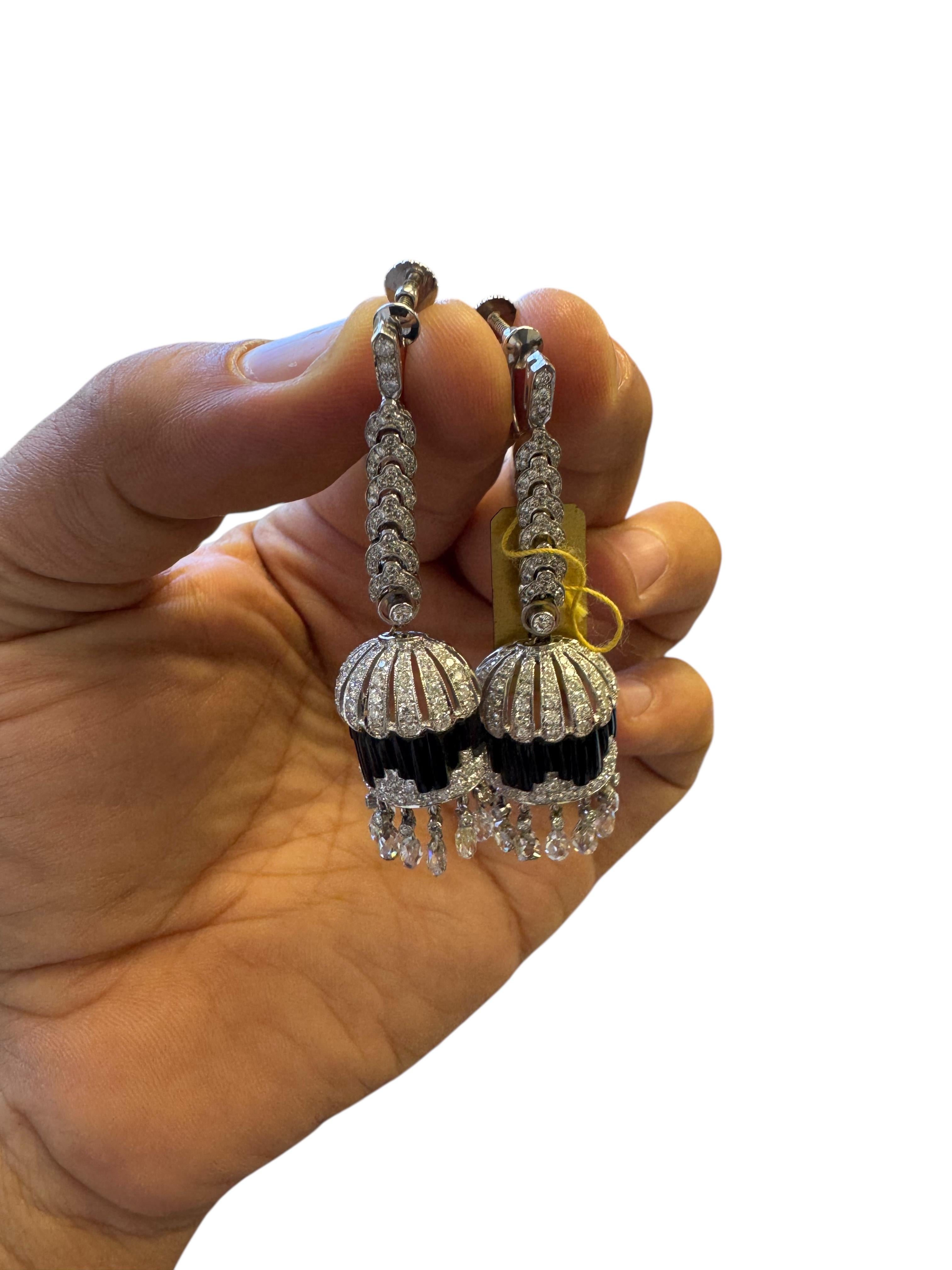 Un sorprendente paio di orecchini in stile Art Déco realizzati in oro bianco 18 carati, con un'affascinante combinazione di onice e diamanti. Ogni orecchino presenta un design architettonico a cupola con baguette verticali di onice bordate da