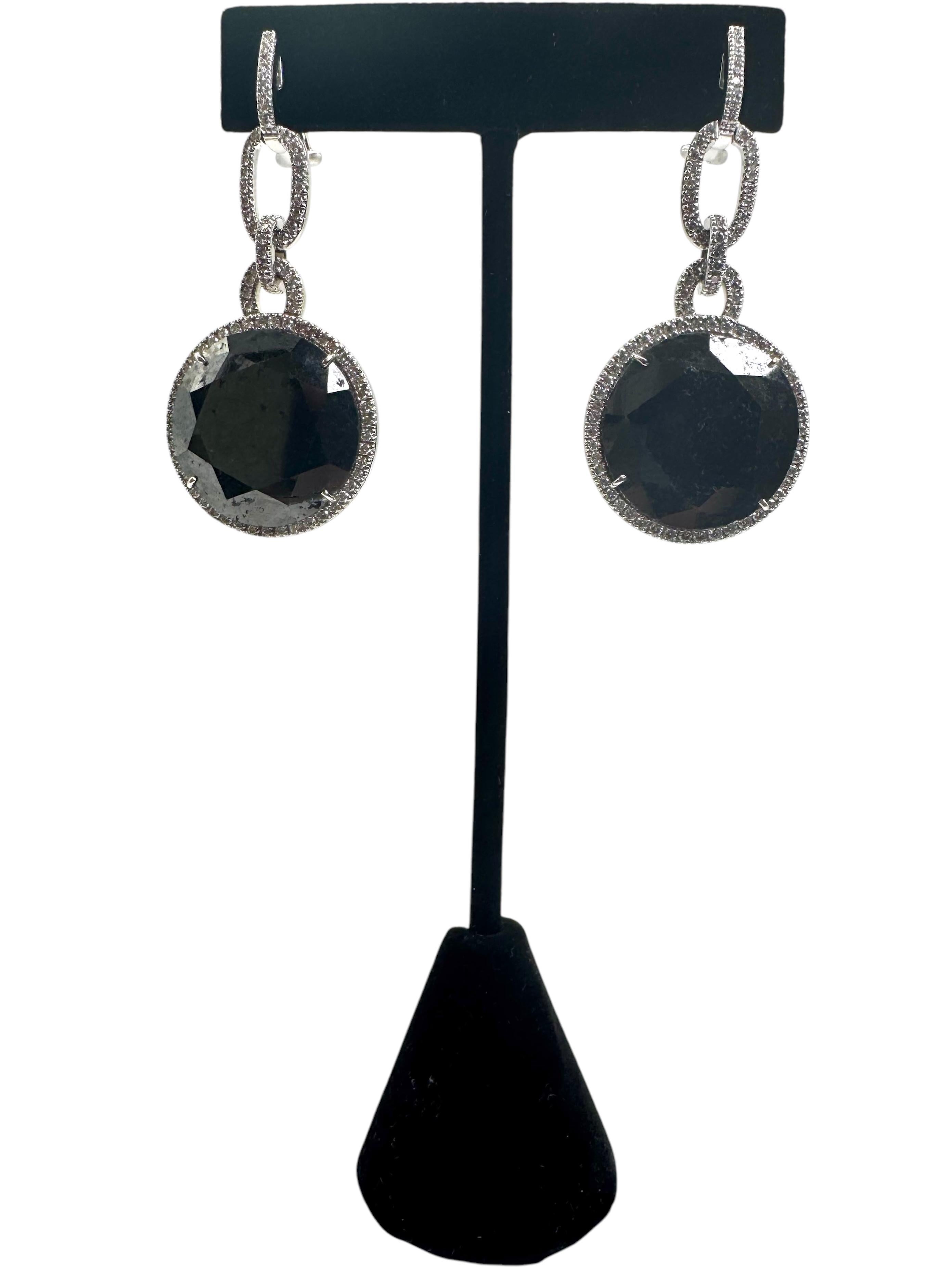 Refined and sophisticated, these stunning drop earrings feature bold round-cut black diamonds suspended from diamond-accented oval links. Crafted in luxurious 18K white gold and marked “750” for authenticity, the design effortlessly combines modern