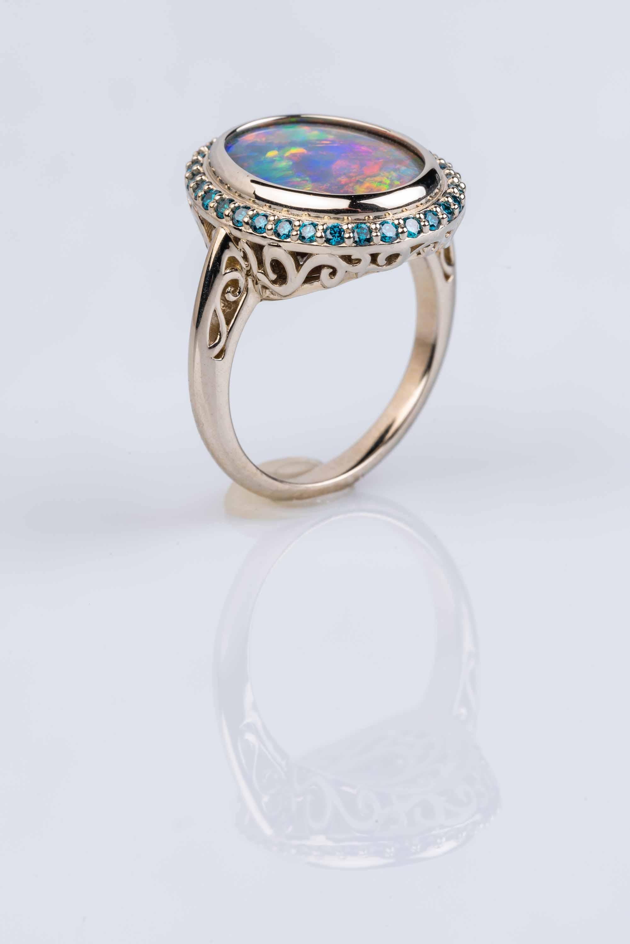 An 18k white gold ring, back-set with a 12.3x15.1mm free form Lightening Ridge Australian black opal, 5.27ct, surrounded by a halo of 32 bead-set 1.5mm teal blue diamonds, 0.40 total carat weight. This ring is a size 7. This ring was made and