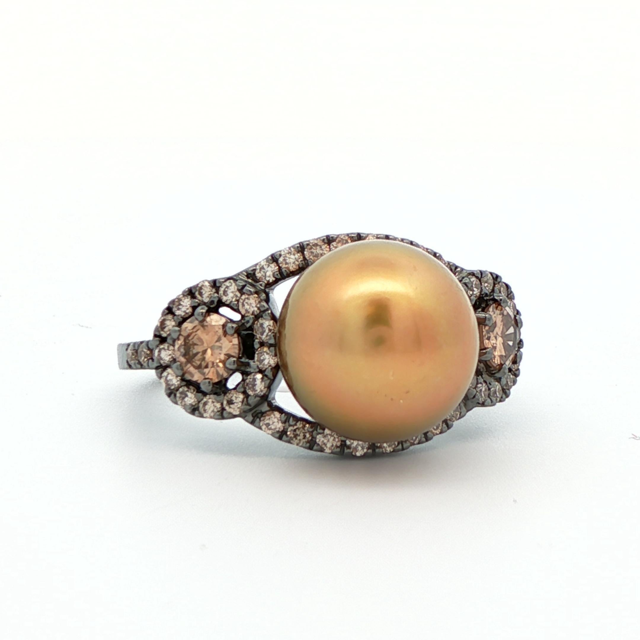 Cette magnifique bague en perles et diamants est réalisée en or blanc 18k avec rhodium noir. Le centre est constitué d'une perle ronde des mers du Sud de couleur or/rose d'une taille d'environ 9,5 à 10 mm. 48 diamants de couleur chocolat entourent