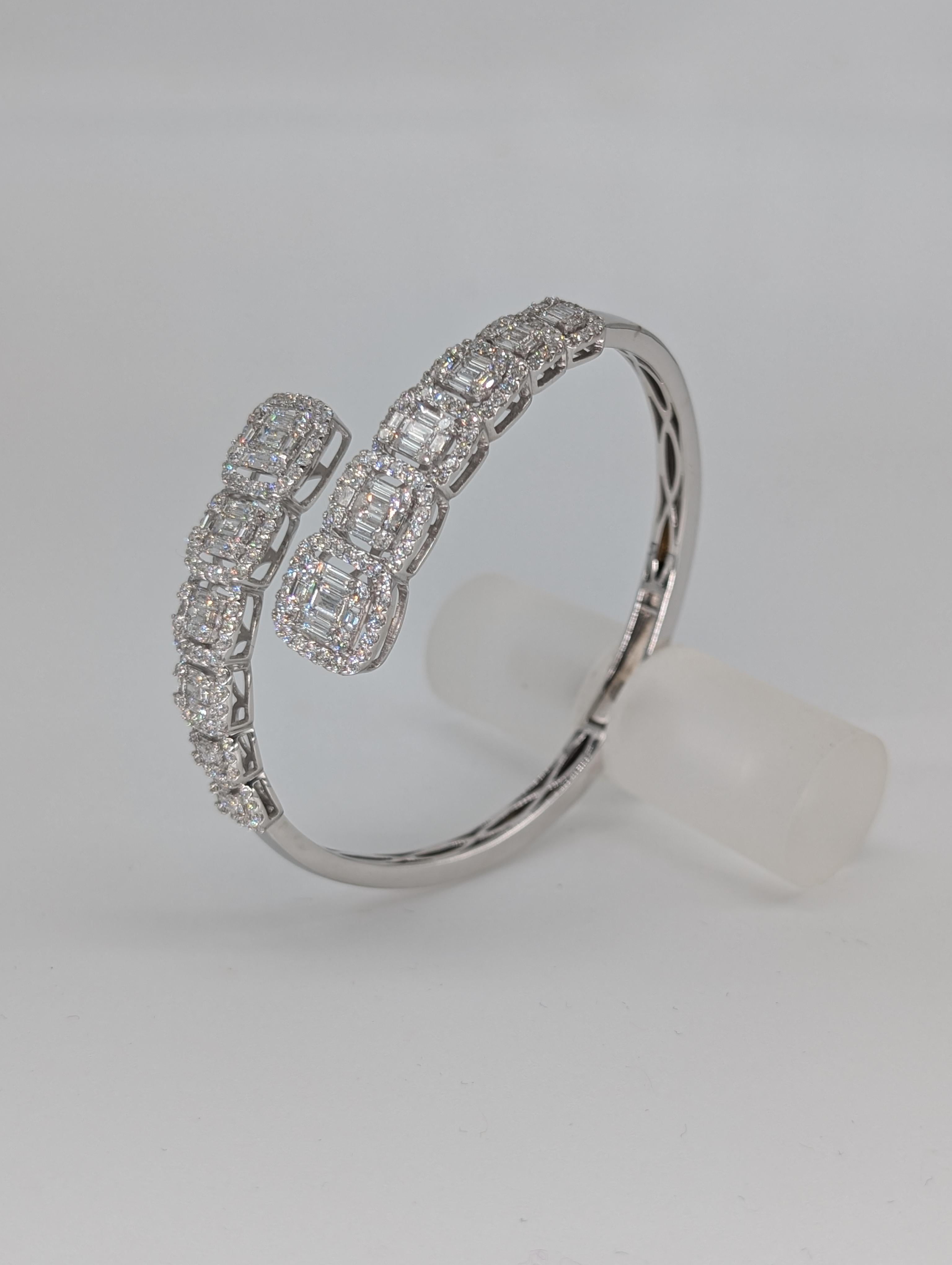 Questo splendido braccialetto bypass in oro bianco 18 carati è un vero e proprio pezzo forte, caratterizzato da un accattivante mix di diamanti a baguette e a taglio rotondo. Con un peso totale di 5,73 carati, i diamanti sono sapientemente