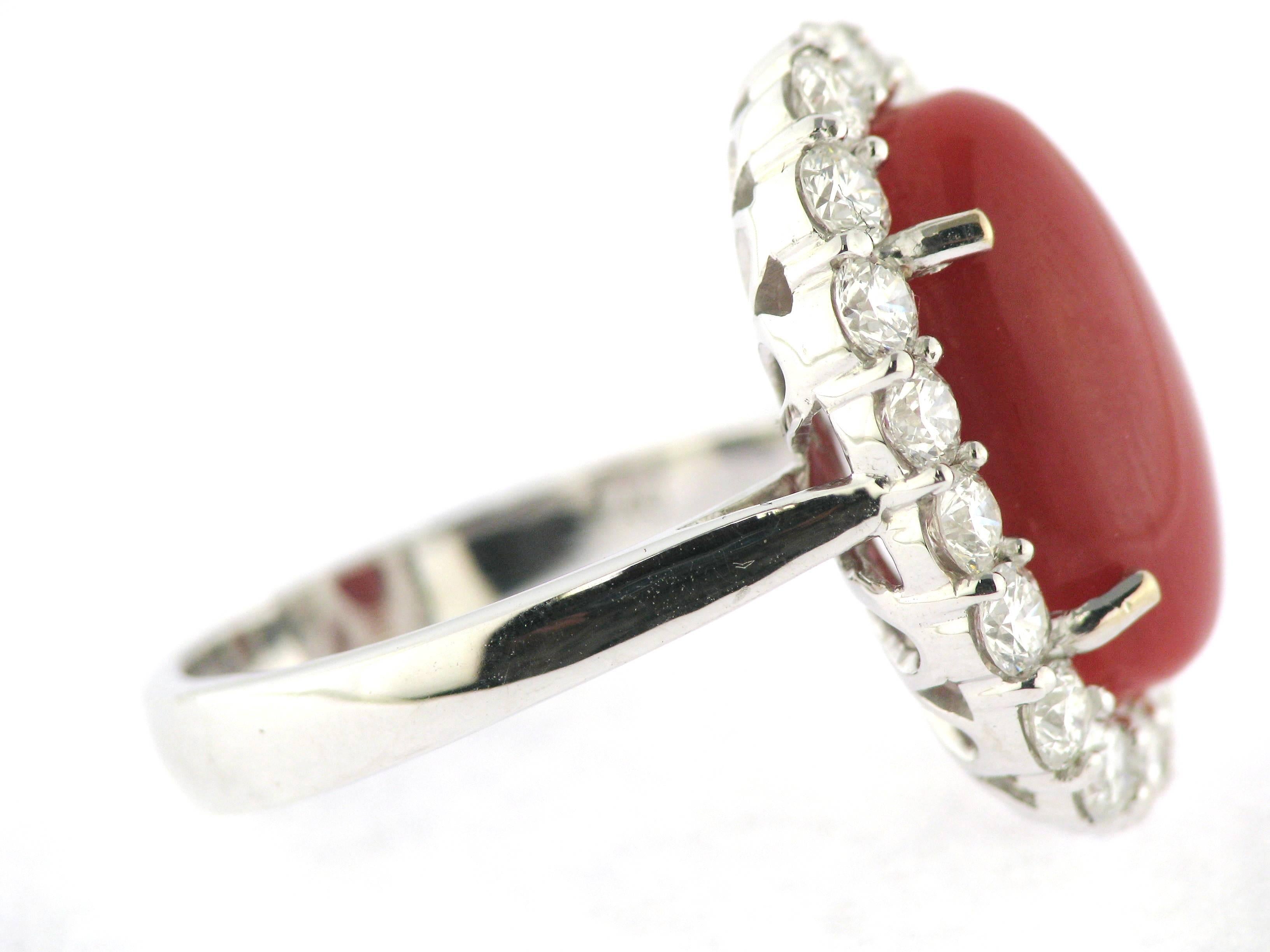 Featuring an 18K white gold cluster ring claw set with a central oval en cabochon cut red (rosso) South China Sea coral 15.3mm x 9.5mm surrounded by 18 Round Brilliant diamond. Total estimated carat weight 1.8  carats. The ring has a rounded shank