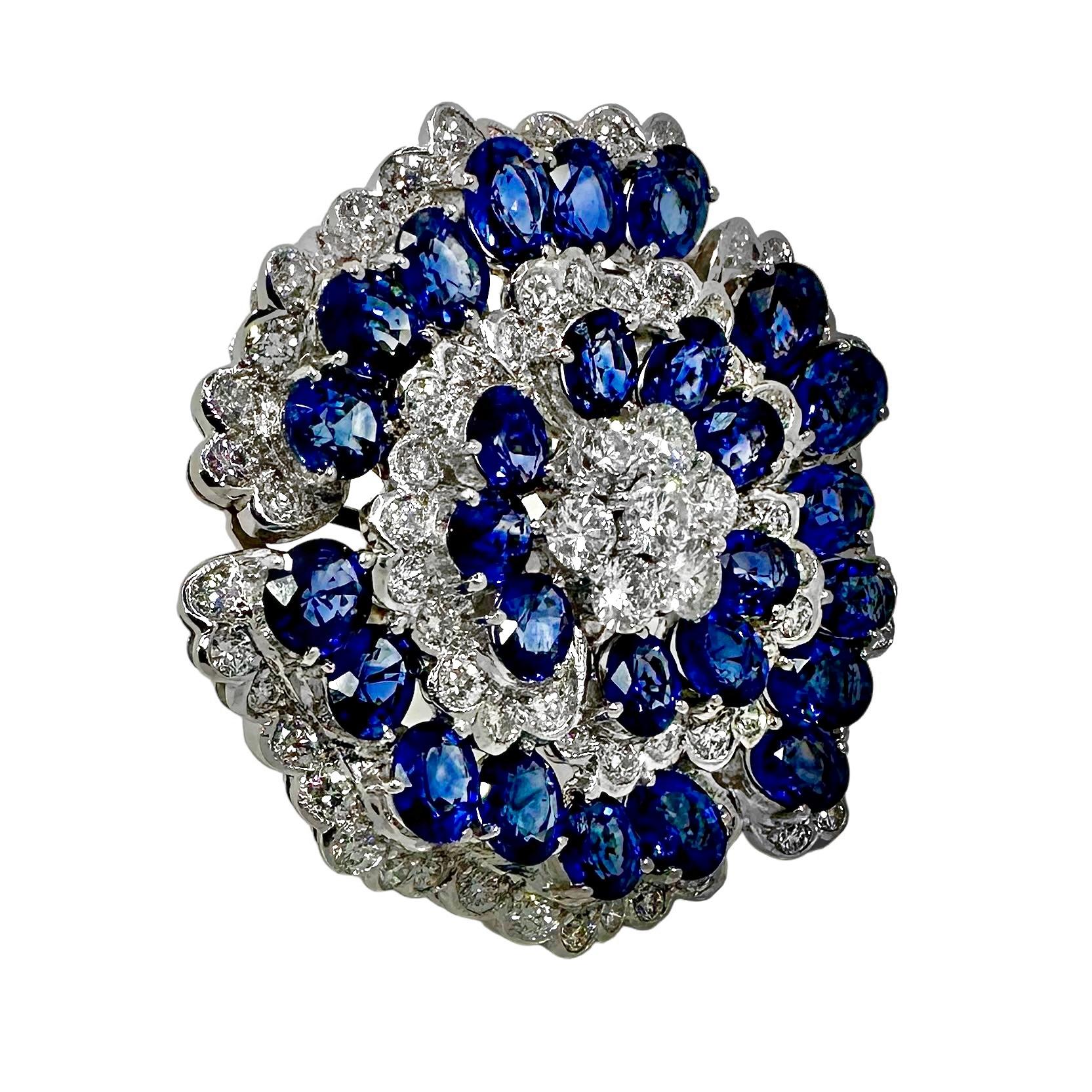 Cette exceptionnelle bague de cocktail vintage pour femme, d'un diamètre de 1 1/2 pouce, est façonnée en or blanc 18 carats, avec des saphirs ovales vifs et des diamants ronds de taille brillant, dans un motif de camélia. En ce qui concerne les