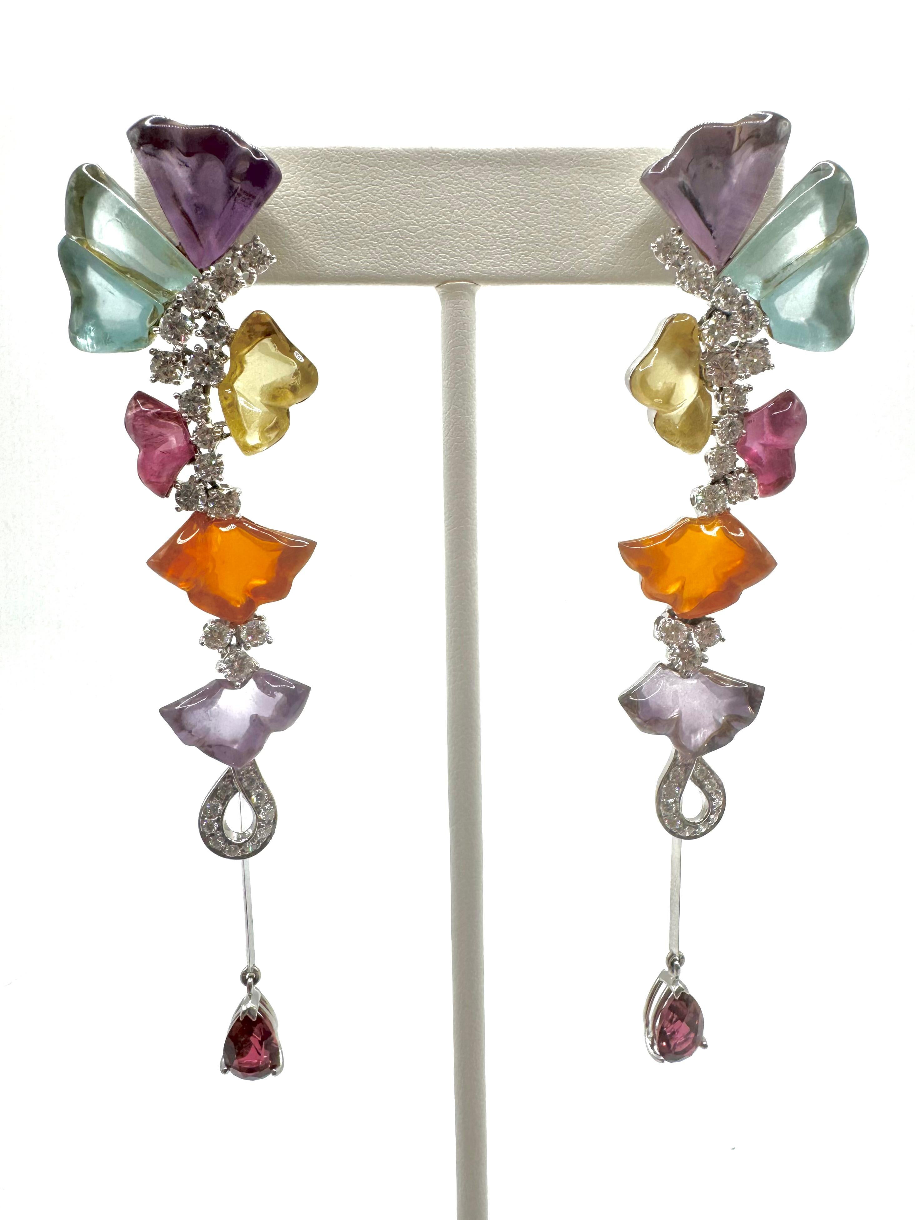 A stunning pair of Italian designer earrings crafted in 18K white gold, featuring a vibrant arrangement of carved heart- and fan-shaped gemstones in shades of amethyst, citrine, aquamarine, pink tourmaline, and orange chalcedony. Sparkling round