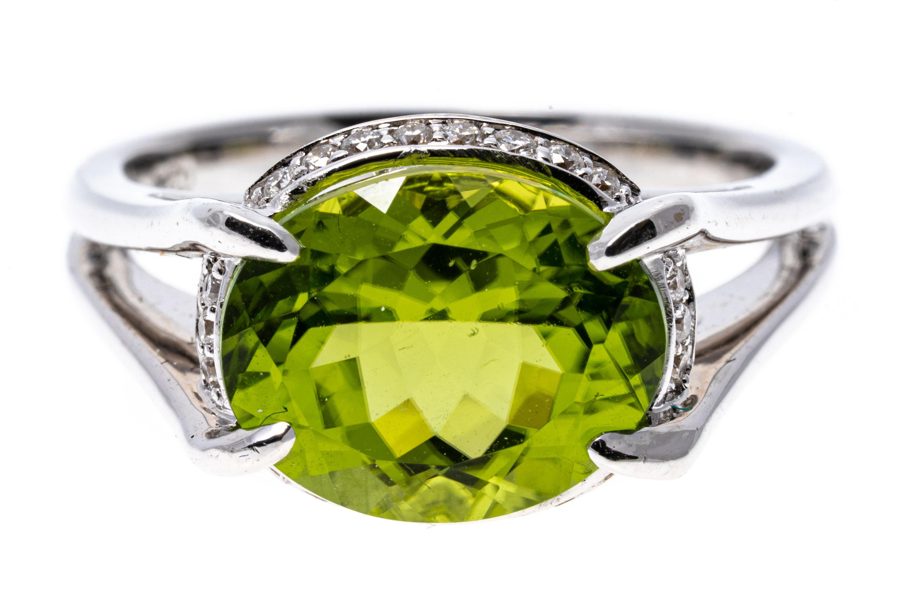 18k white gold ring. This handsome contemporary ring is a horizontal, oval faceted, chartreuse green color peridot, approximately 3.81 CTS, prong set and decorated with a round faceted diamond halo gallery, approximately 0.05 TCW. The ring is
