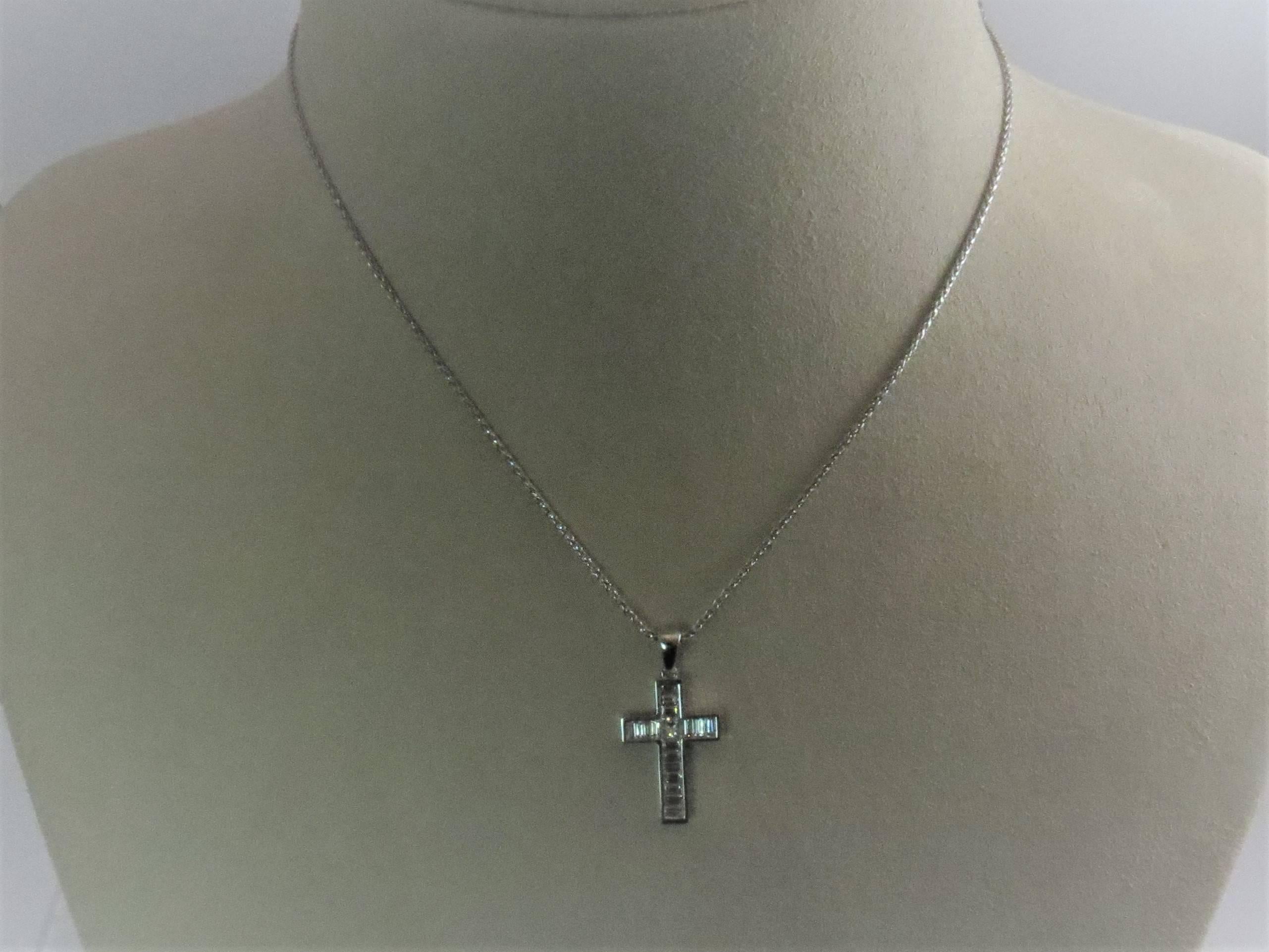 18K white gold cross, channel set with 16 baguette diamonds and one princess cut diamond, G-H color, VS color weighing 1.02cts total suspended from 16 inch 18K white gold chain.