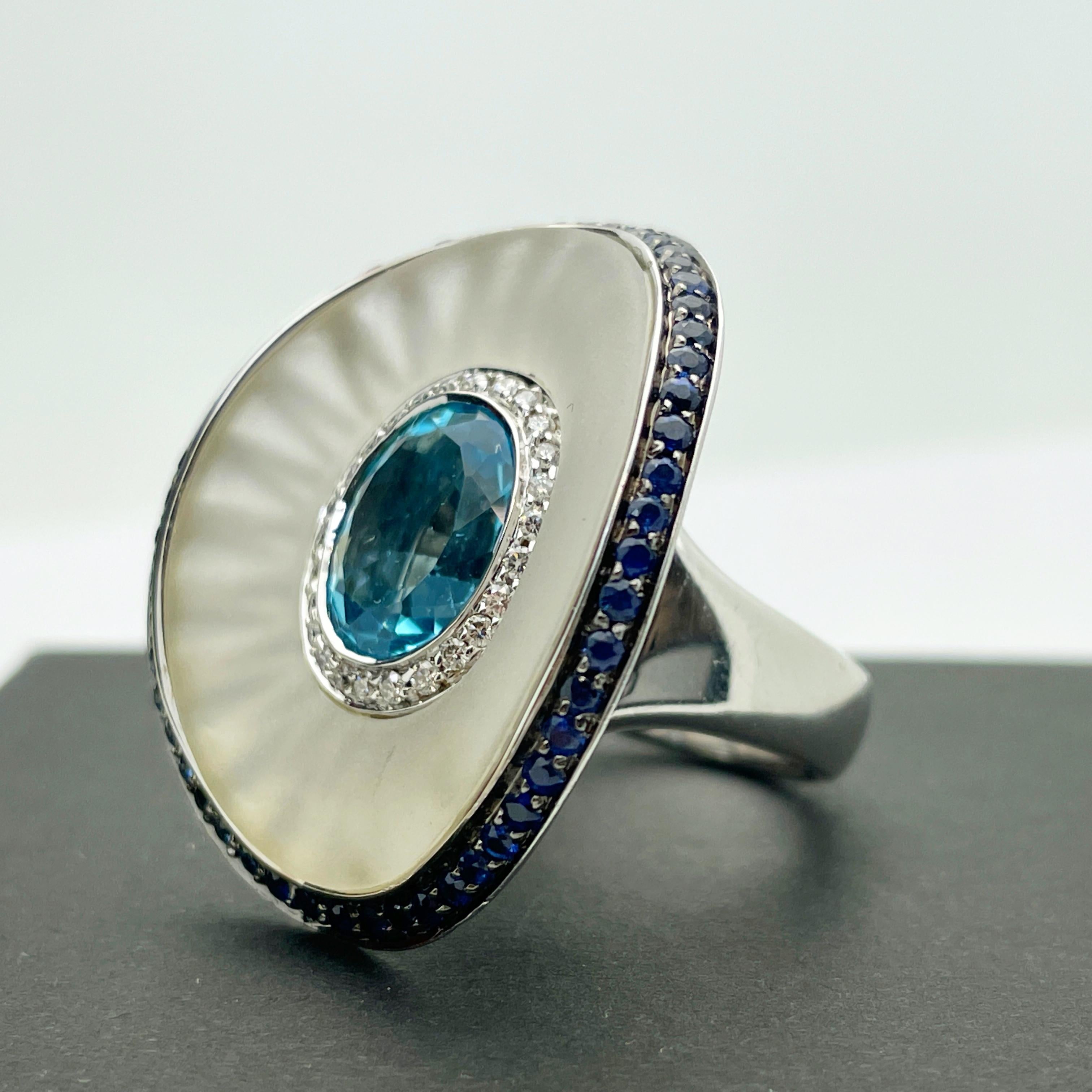 Here is a stunning Italian Custom Made 18k Large White Gold Custom Made Blue Topaz, Diamond, Rock Crystal and Sapphire Ring.

This heavy and substantial ring features a 6.00ct oval cut blue topaz measuring approx. 12.00mm x 10.00mm. The topaz is