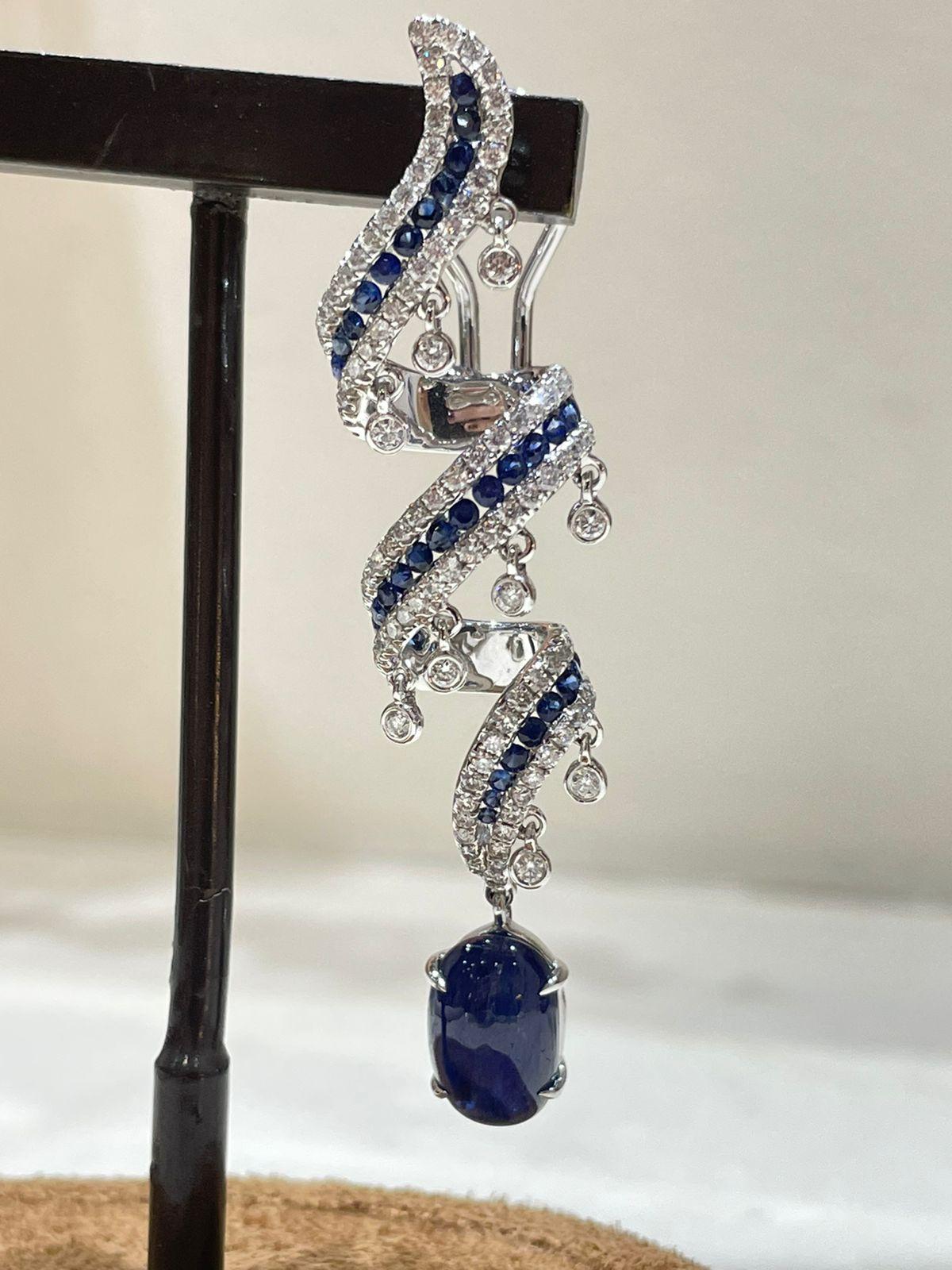These dangling earrings exude sophistication and elegance with a perfect balance of simplicity and opulence. A striking blue sapphire takes the stage adorned with exquisitely round-cut diamonds. The design ensures a reflection of light and glamour