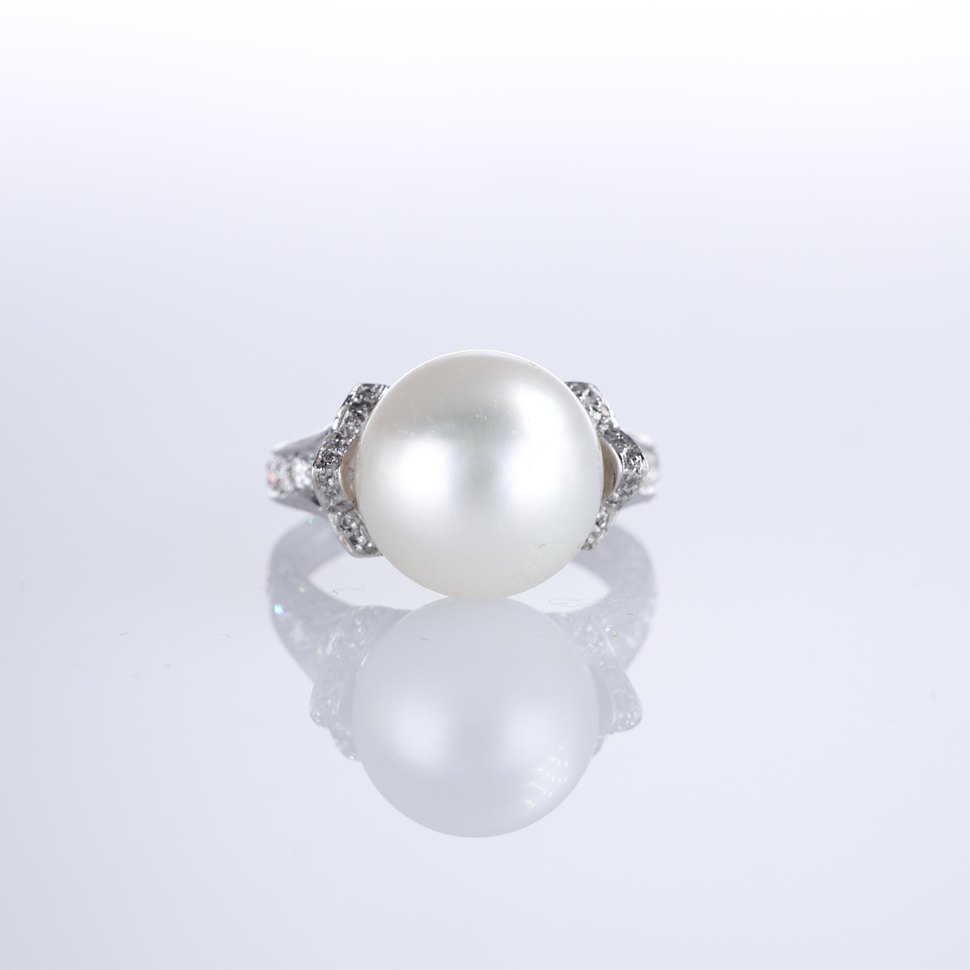 An exquisite 18K white gold ring featuring a luminous central white pearl, accentuated by a band adorned with natural brilliant-cut diamonds. A delicate clover-shaped diamond arrangement on each side adds a refined touch, enhancing the timeless