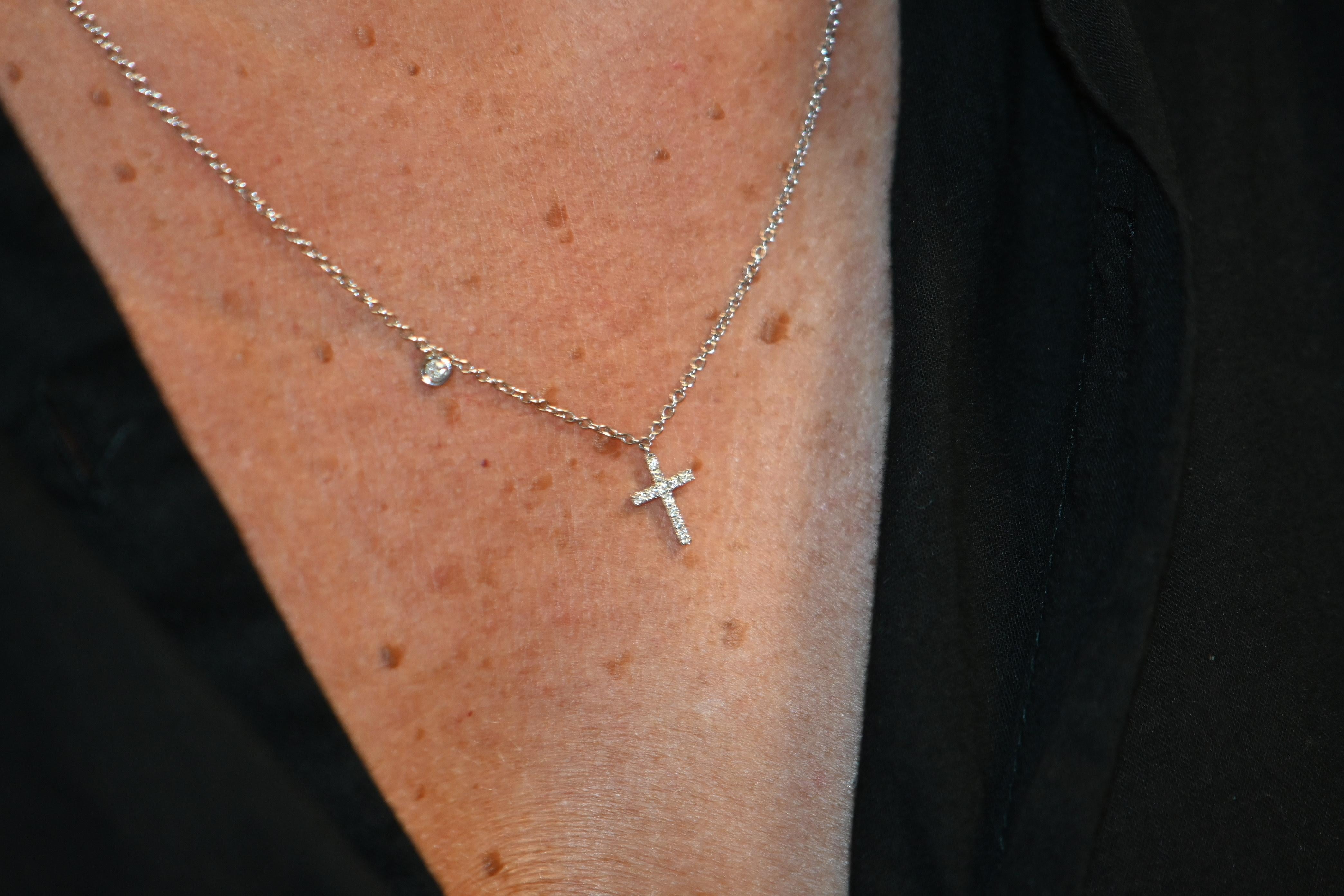 This delicate necklace is crafted in 18 karat white gold and features a minimalist yet elegant cross pendant, pavé-set with brilliant-cut diamonds for a subtle sparkle. A single bezel-set diamond is set asymmetrically on the chain, adding a