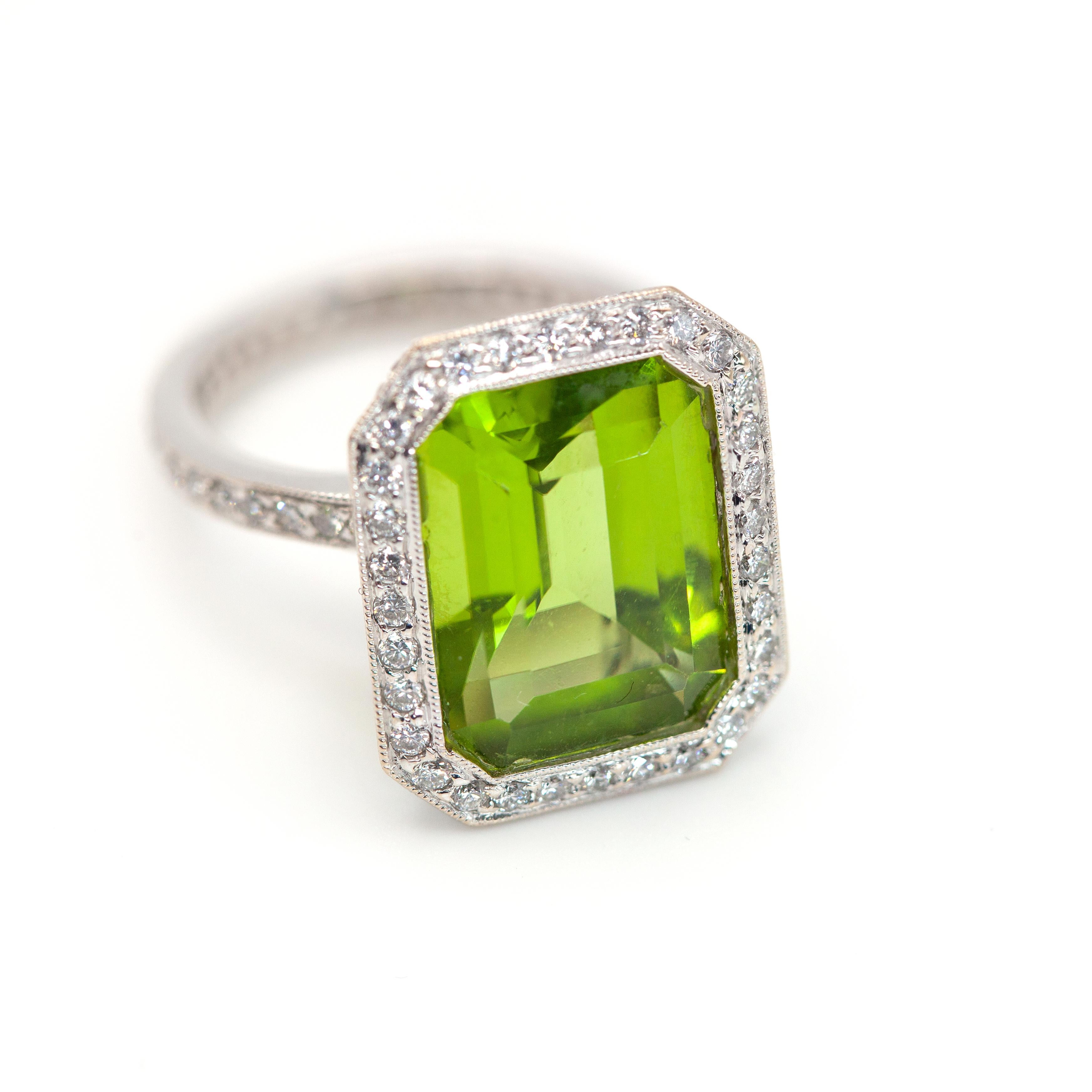 Questo splendido anello da cocktail con diamante e peridoto in oro bianco 18K contiene un peridoto di buona qualità dal taglio smeraldo di circa 8,20 carati, circondato da diamanti rotondi dal taglio brillante e incastonato in un castone con