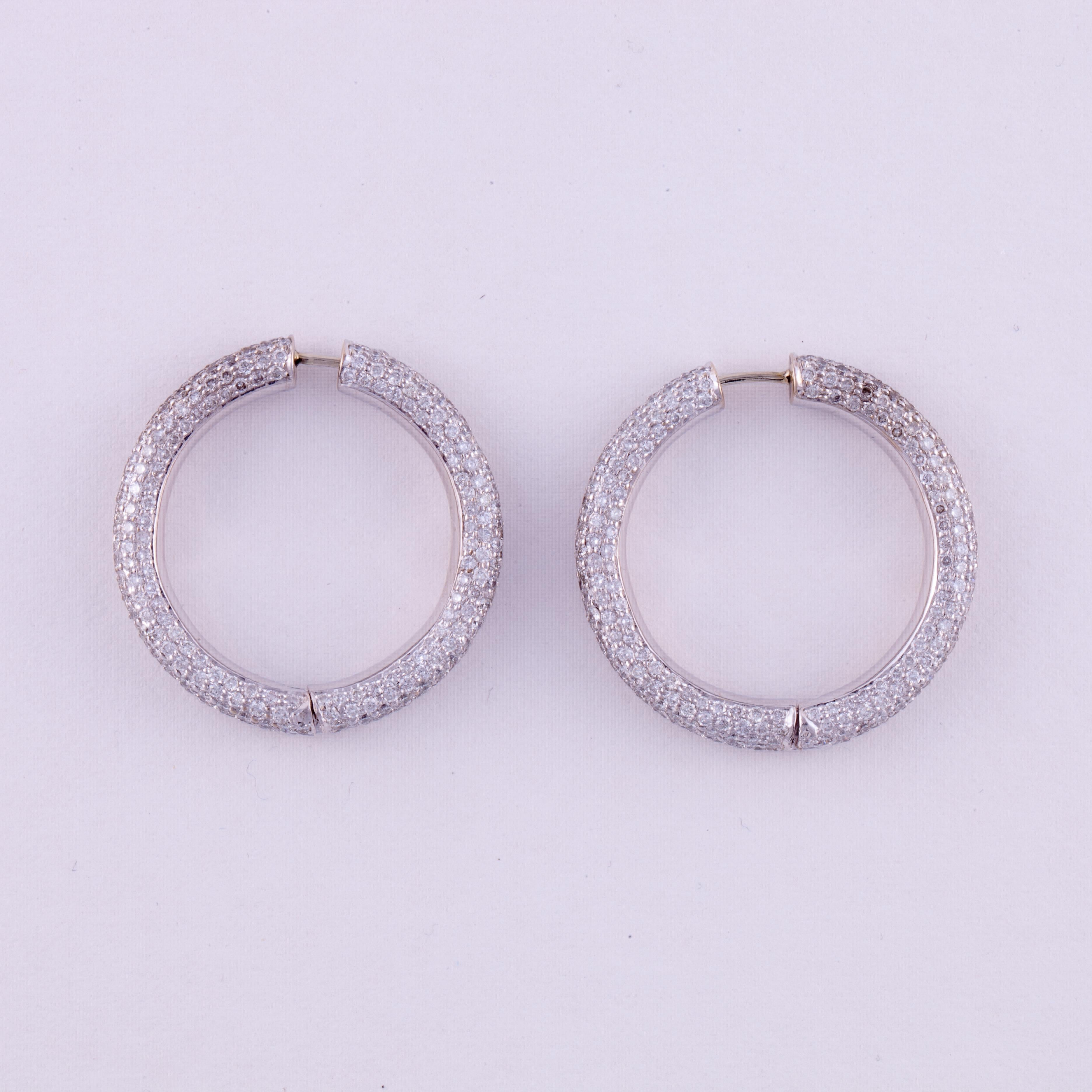 Pavé diamond hoop earrings in 18K white gold.  There are 10.25 carats of round brilliant-cut diamonds; H-I color and SI1-I1 clarity.  They measure 1 1/4 inches across and 3/16 inches wide. 