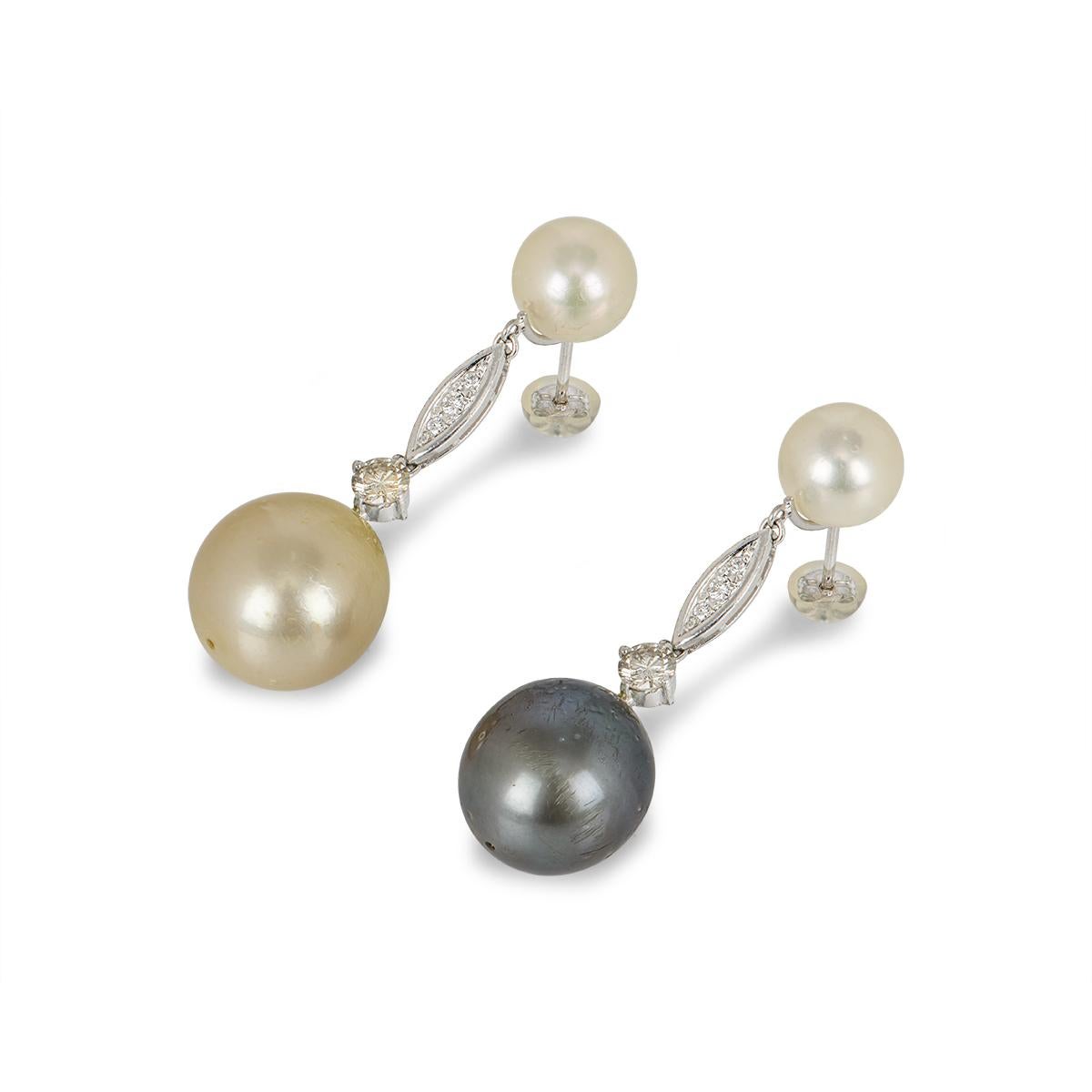 A pair of 18k white gold pearl and diamond drop earrings. Each earring is composed of a 9mm white pearl from which has a pave set diamond detailing that leads to a single round brilliant cut diamond. Suspended from the single diamond is a larger