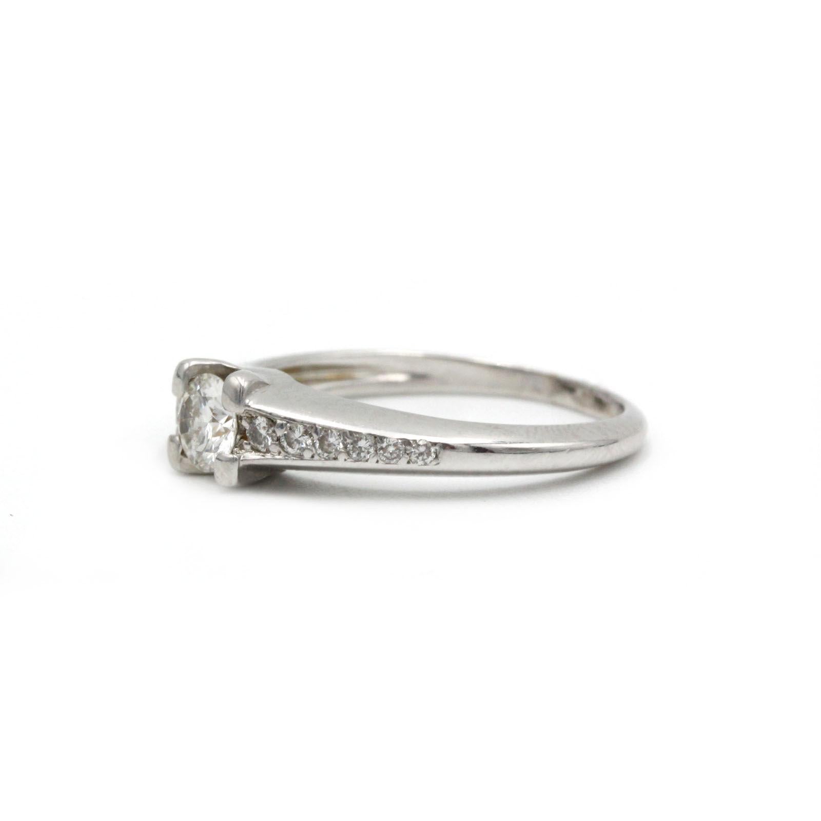 Questo elegante anello in oro bianco 18 carati presenta un diamante rotondo brillante da 0,40 carati al centro, affiancato da dodici diamanti d'accento con taglio brillante per un totale di circa 0,25 carati. La fascia elegante e lucida si