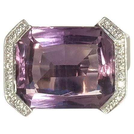 This 18k white gold ring is adorned with a rectangular, faceted amethyst which is mounted by 26 sparkling brilliant cut diamonds. The shank of the ring is wide and its setting powerfully shaped with two prominent shoulders holding the gorgeous