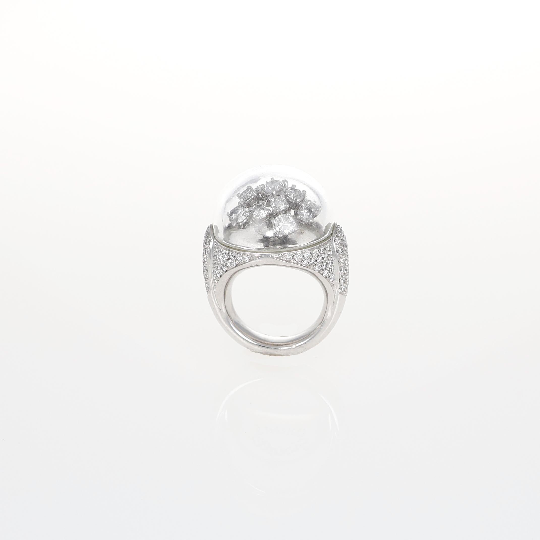 Questo anello in oro bianco 18 carati, dal design audace e innovativo, presenta una sorprendente struttura a cupola con una parte superiore in cristallo trasparente, che racchiude una delicata composizione floreale di diamanti. L'effetto fluttuante
