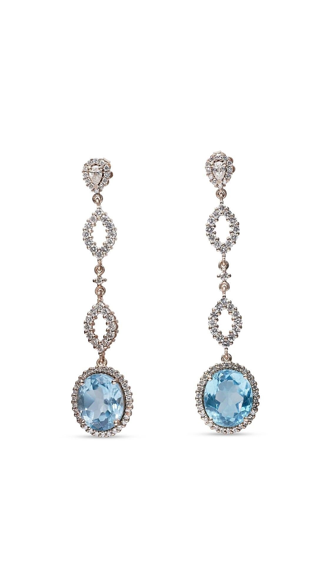 A beautiful pair of halo drop earrings with a dazzling pair of 14.80 carat oval natural blue topaz. It has 2.57 carat of side diamonds, which add more to their elegance. The jewelry is made of 18K white gold with a high quality polish. It comes with