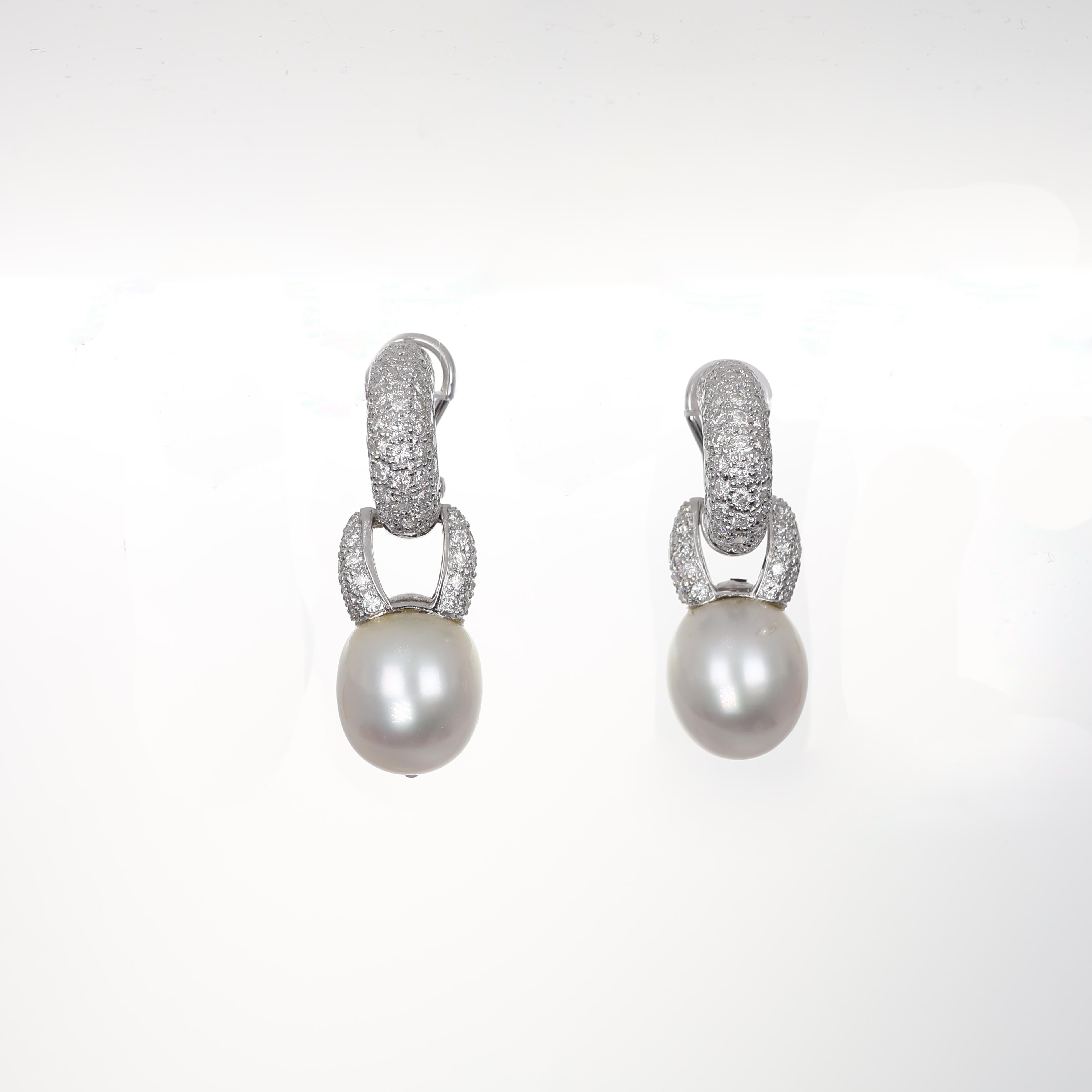 A striking pair of 18K white gold drop earrings featuring luminous pearls suspended from a refined diamond pavé setting. The intricate craftsmanship enhances the brilliance of the diamonds, creating a luxurious contrast with the smooth pearls. A