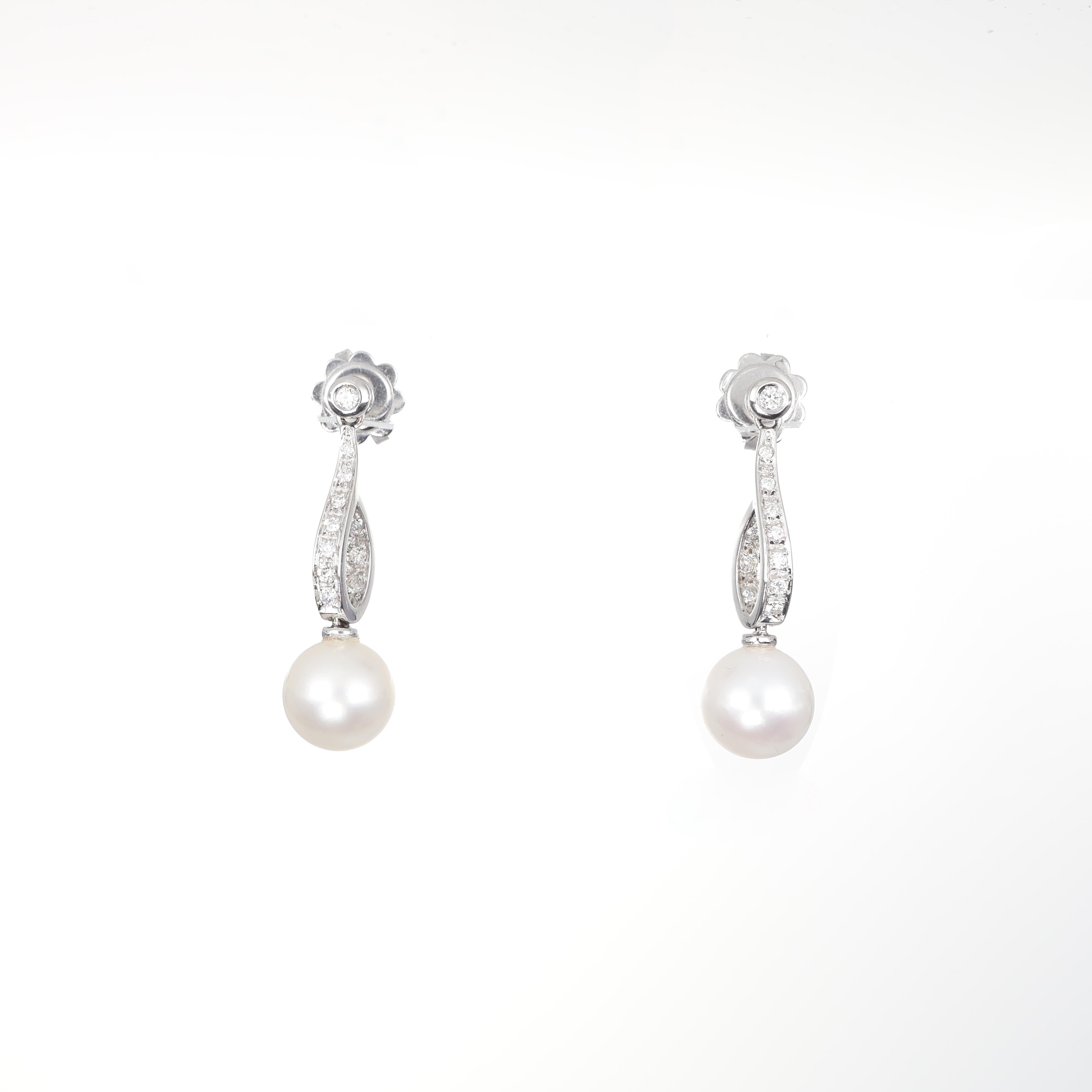 Graceful and refined, these 18K white gold drop earrings feature luminous pearls suspended from an elegantly curved bar adorned with pavé-set brilliant-cut diamonds. The delicate sparkle of 0.19 carats of diamonds enhances the natural radiance of