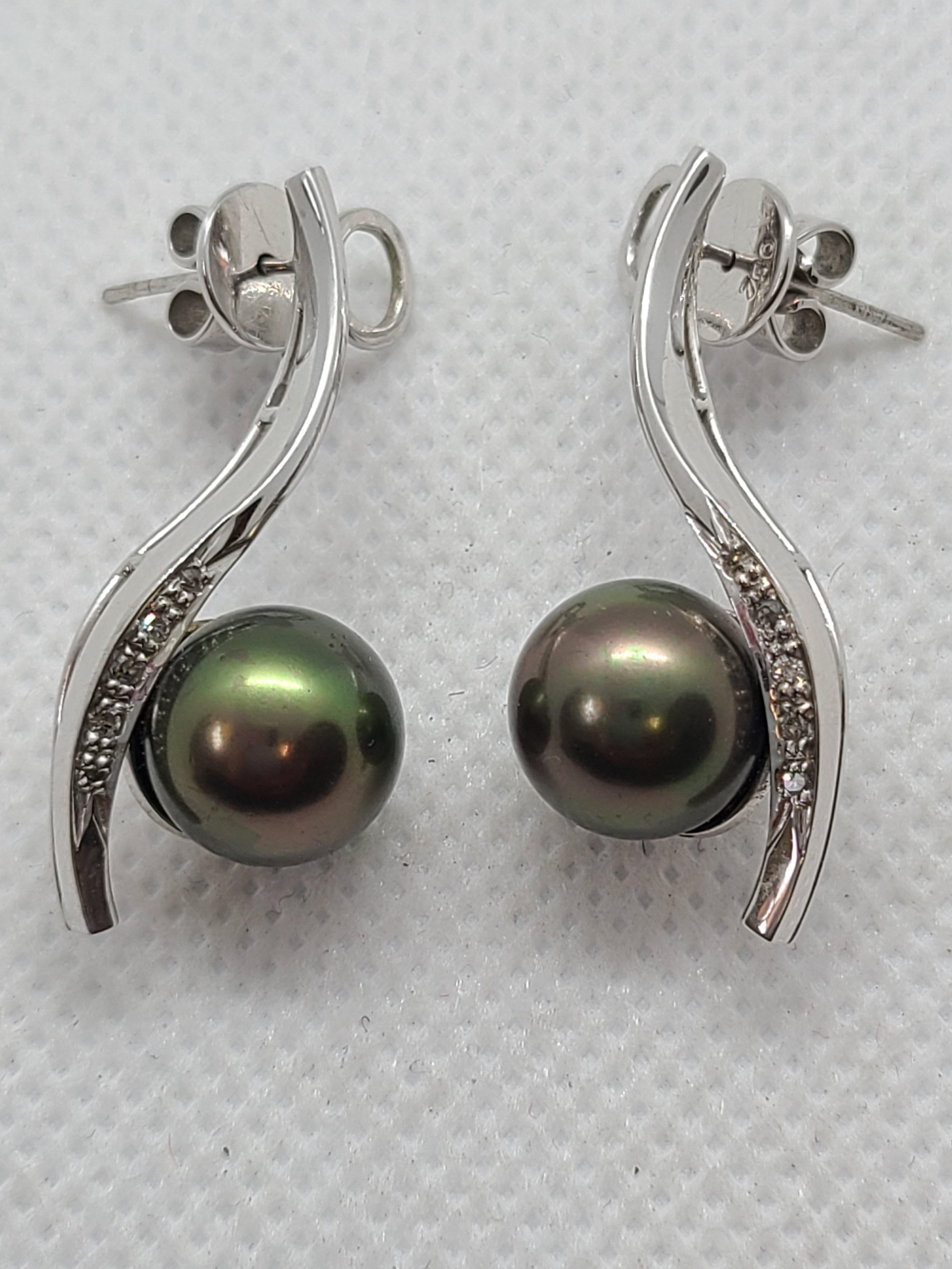 Un paio di orecchini di perle nere di Tahiti coltivate, realizzati a mano, con una perla di 10 mm splendidamente lucente incastonata in un elegante oro bianco 18 carati. Le perle sono completate da diamanti rotondi scintillanti, che esaltano la