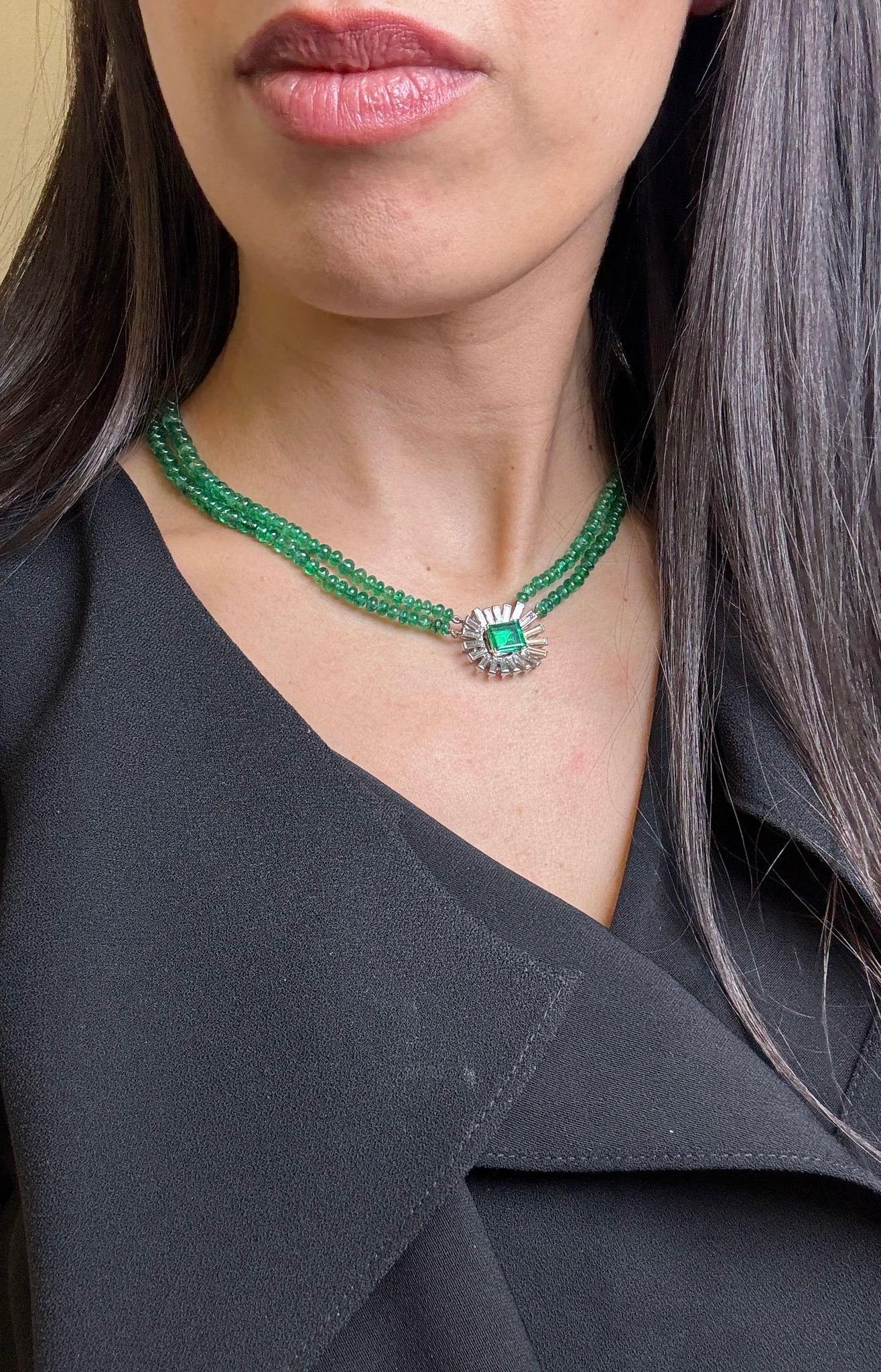 A striking vintage necklace featuring two strands of richly saturated emerald beads, finished with a bold emerald-cut emerald centerpiece framed by a radiating halo of tapered baguette-cut diamonds. The clasp and setting are crafted in 18K white