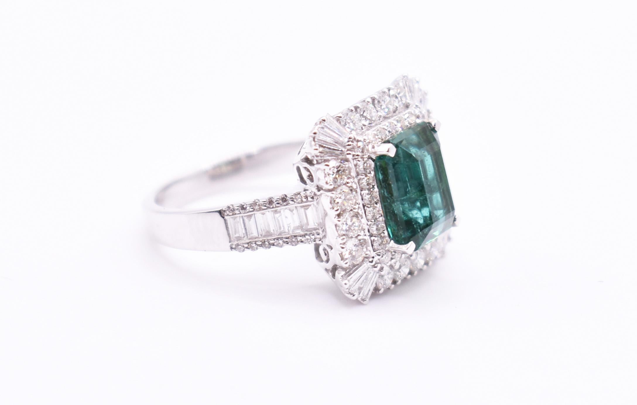 A beautiful 18k white gold emerald & diamond ring, featuring an emerald cut Zambian emerald in a prong setting, edged by a large quantity of diamonds, over a straight shank, with further round and baguette cut diamonds. Emerald = 2.81ct Diamonds =