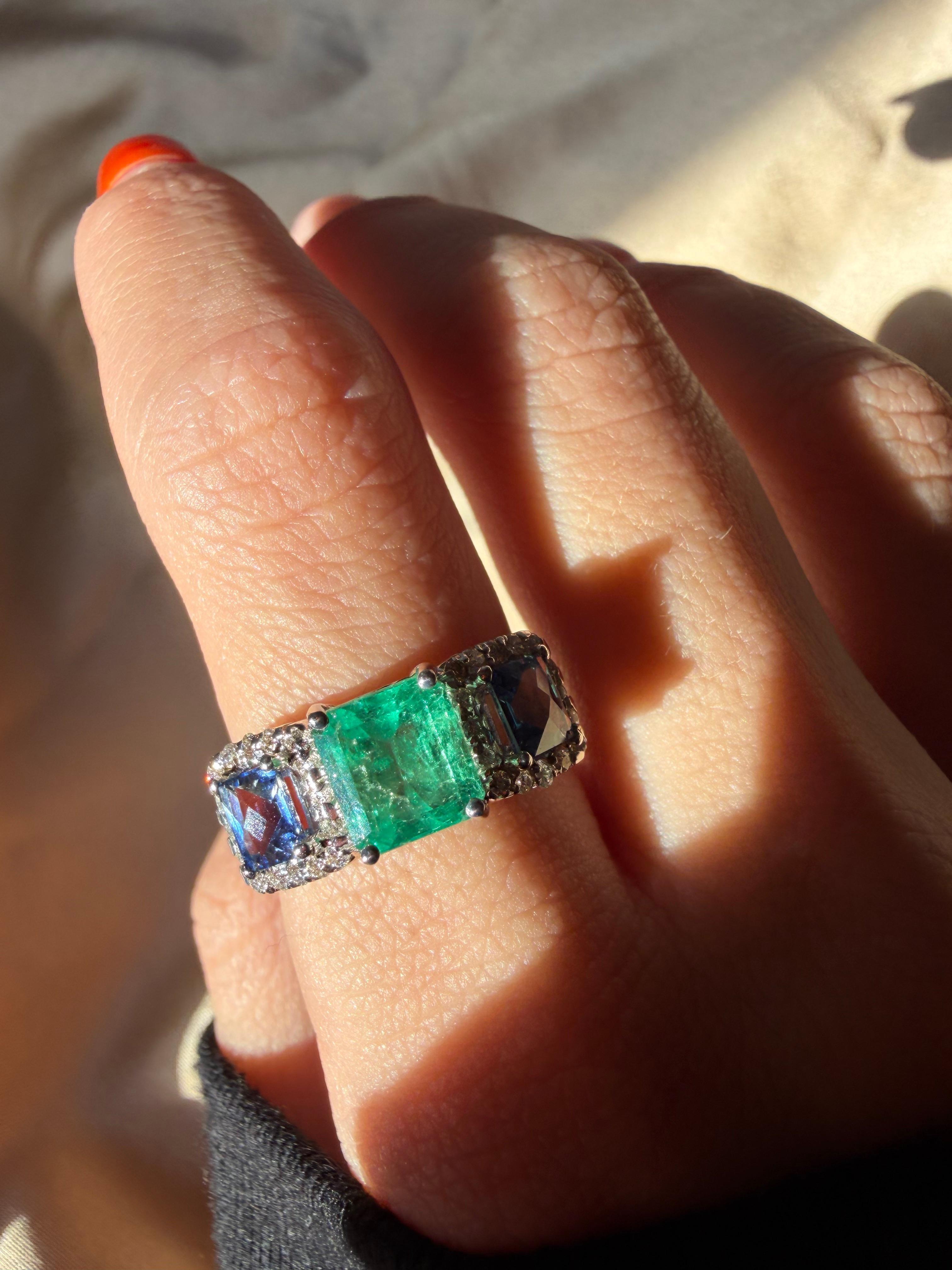 Cette bague à large bande présente une émeraude de 1,66 carat au centre, encadrée par deux saphirs de 1,26 carat au total. Le trio de pierres est rehaussé de diamants ronds brillants étincelants totalisant 0,29 carat, ajoutant une dimension et un