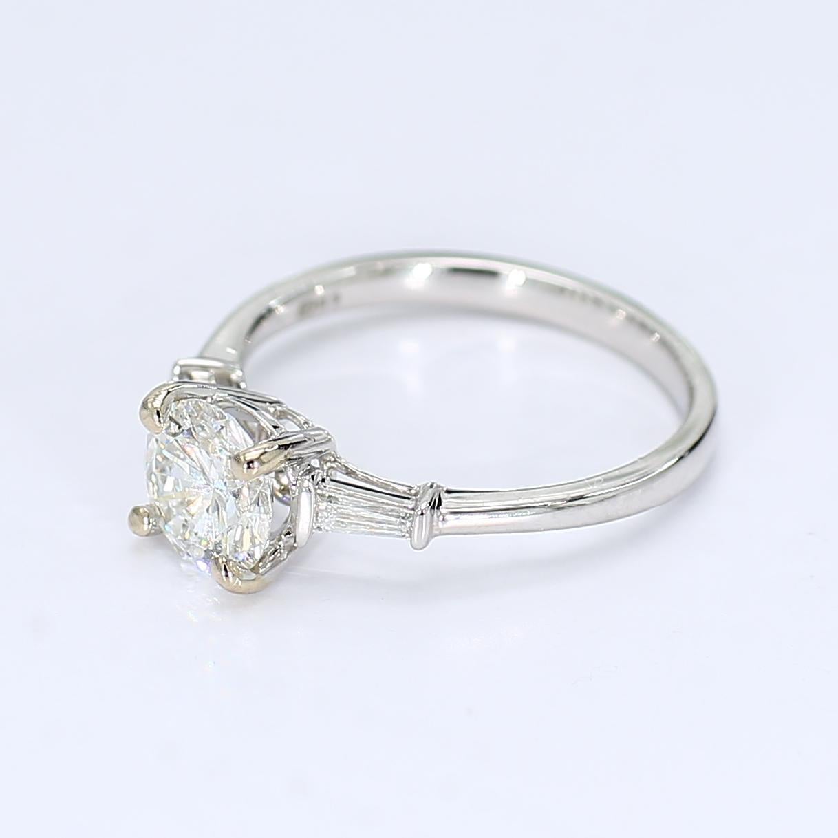 Il s'agit d'une belle bague de fiançailles classique mais discrète. Il abrite un diamant rond central de ~1,28ct (SI2/G) flanqué de part et d'autre de deux diamants baguettes effilés de ~0,029ct (VS2/F). Une bague magnifique qui résistera à