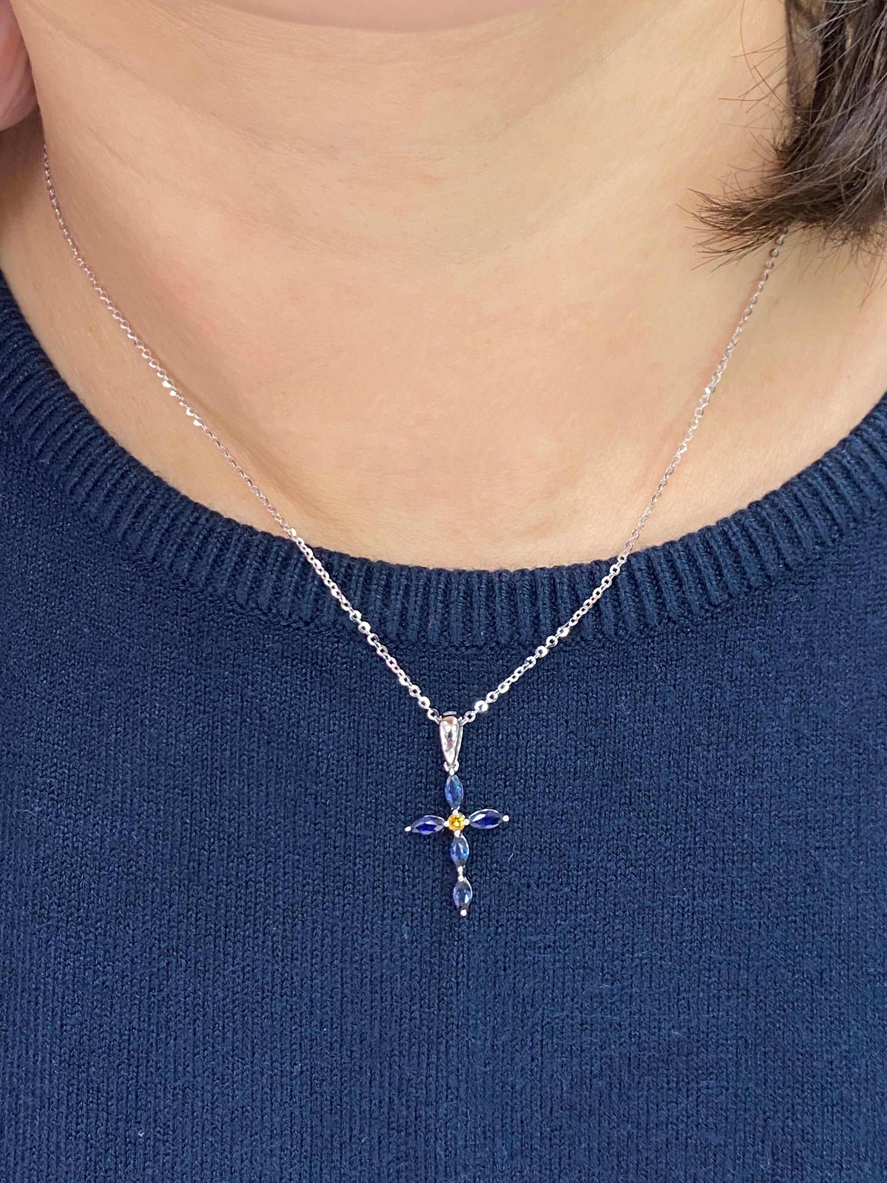 This is a beautiful classic cross pendant. It is set in 18k white gold and one fancy vivid yellow diamond. In the center is one fancy vivid yellow diamond. There are 5 Marquis shaped royal blue sapphires makeup this cross. The vivid yellow diamond