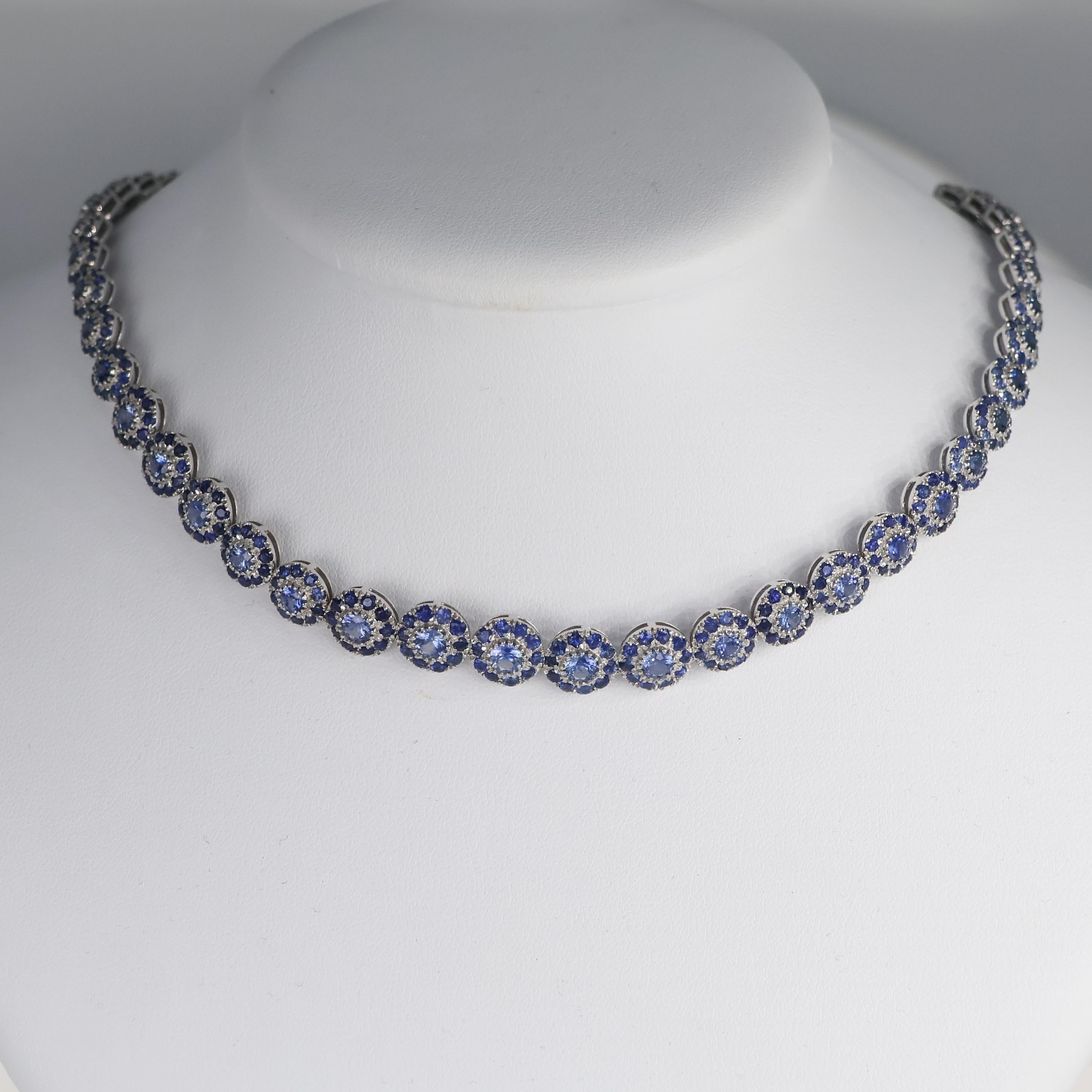 A delicate yet striking floral choker necklace, crafted in 18K white gold and adorned with 20.35 carats of natural blue sapphires. Each link is designed as a blooming flower, with sapphires arranged in a harmonious composition that enhances their