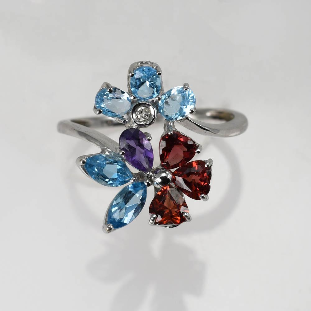 Anello da donna con design floreale e pietre preziose in oro bianco 18 carati.
Timbro 750 e peso di 3,1 grammi.
Ci sono topazi blu ovali e a forma di marquise, granati a forma di cuore, ametiste a forma di pera e un piccolo diamante.
La parte