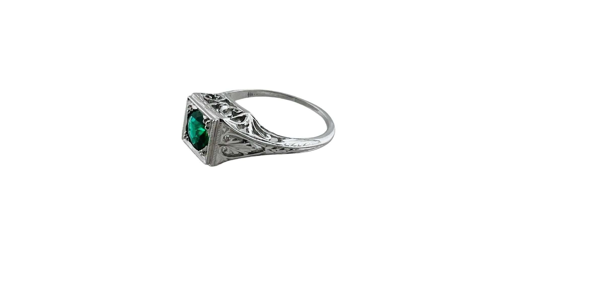 This beautiful white gold ring has a filigree design and a square dome accented with a scroll and leaf design.

Center faceted stone is a round green garnet and glass doublet

Stamped 18K

Shank is approx. 1mm

Front of ring is approx. 7.3 x 8.0 x