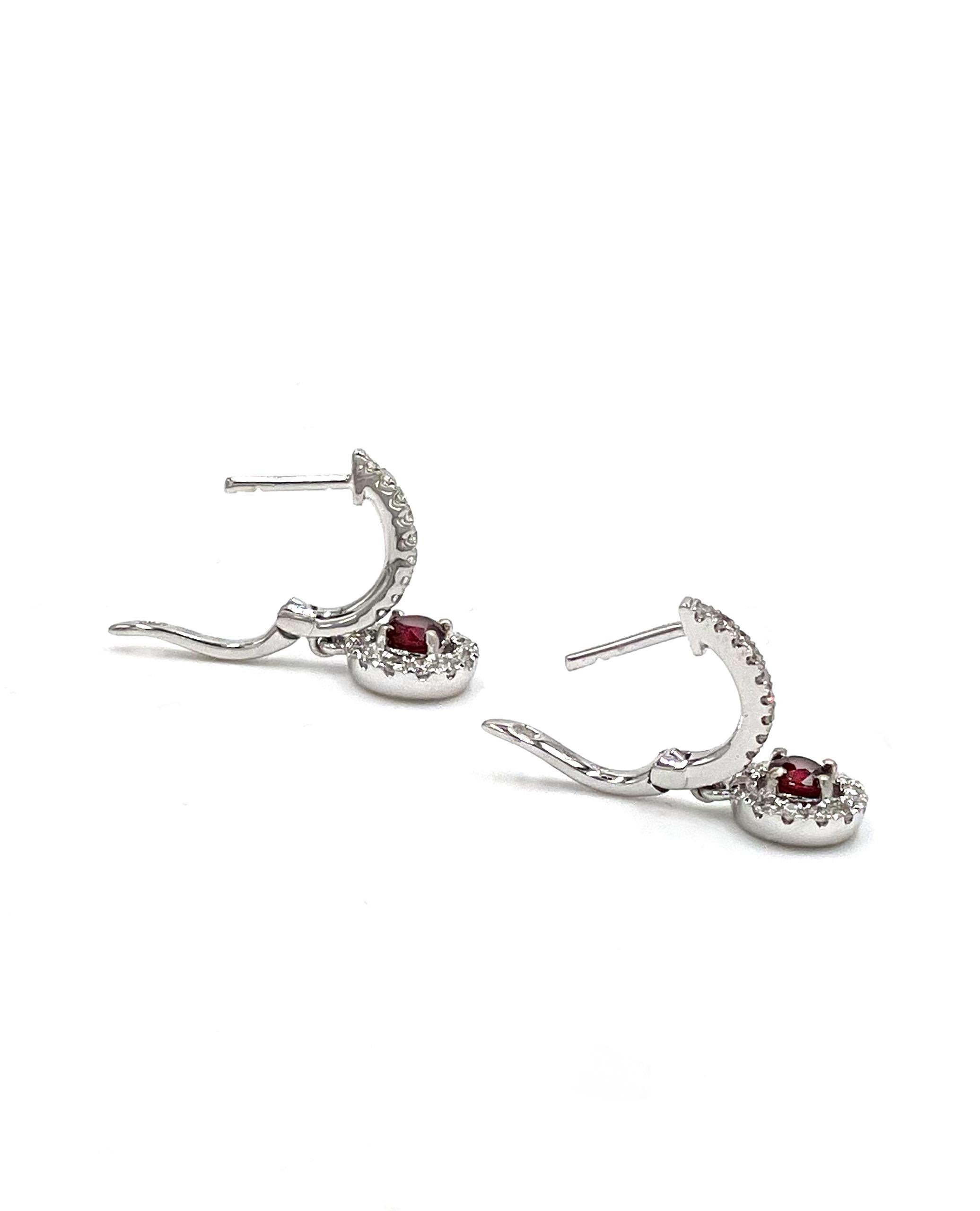 Pair of 18K white gold huggie hoop earrings with hanging halo ruby drops. The earrings are furnished with 44 round diamonds 0.40 carats and two round faceted rubies 0.44 carats.