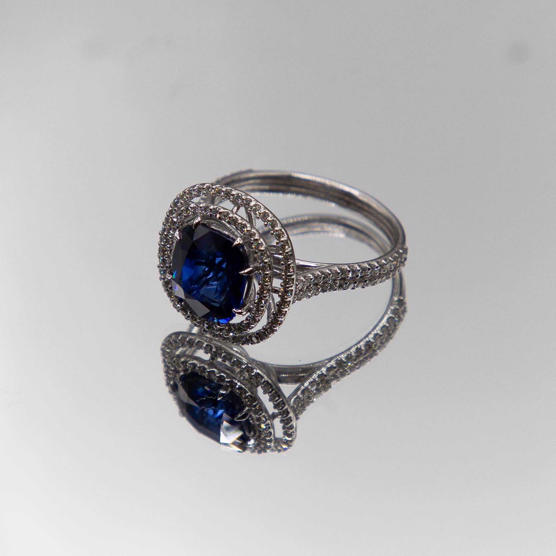 Videography, even at it's best, still misses the true intensity and purity of this rich blue 6.39 carat, cushion- cut Ceylon sapphire. The center gem rests securely, expertly set in a bezel featuring 8 talon-shaped prongs. A double halo, micro-set