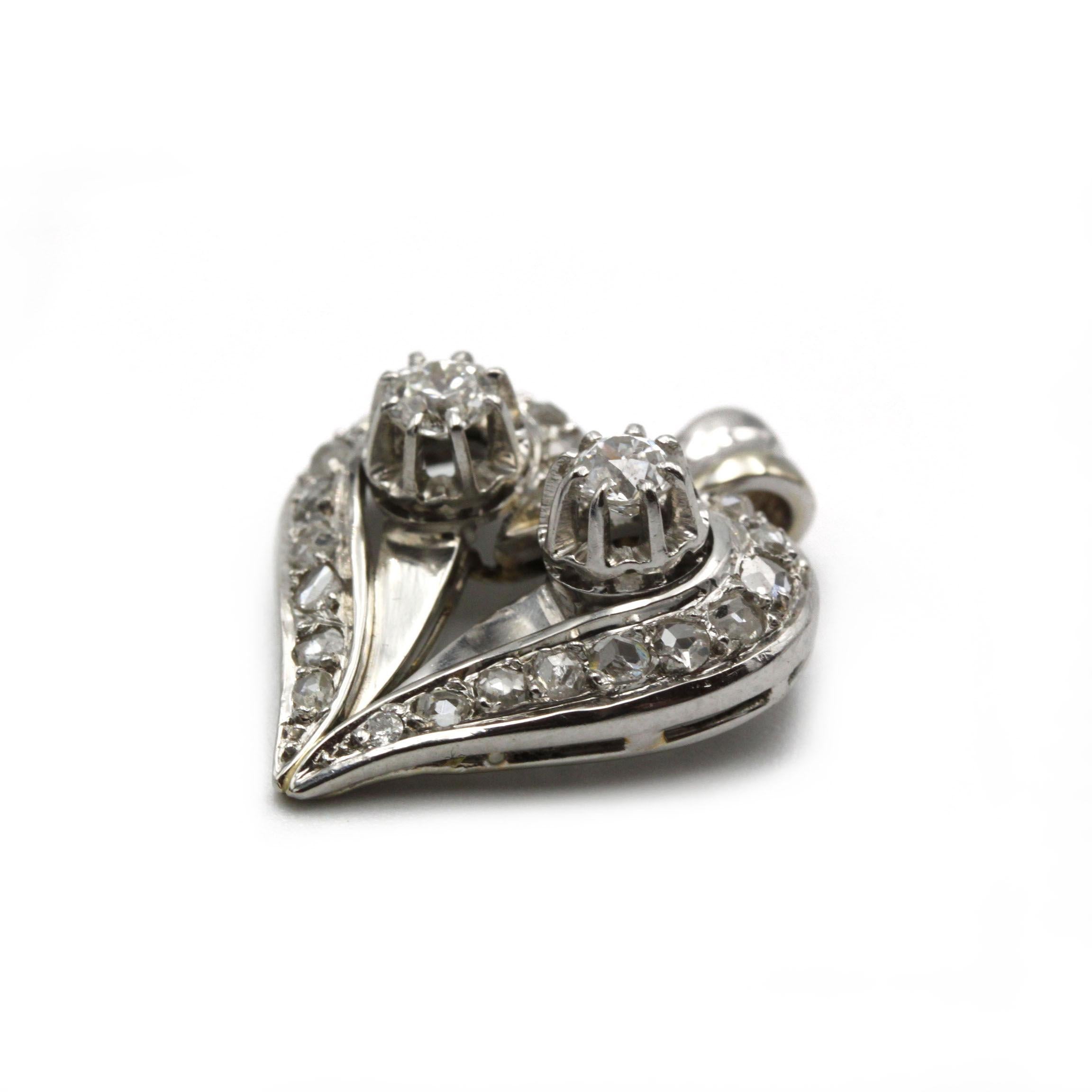 Réalisé en or blanc 18 carats, ce pendentif en forme de cœur est orné en son centre de deux diamants taille brillant d'une valeur totale d'environ 0,40 carat, encadrés par 22 diamants taille rose étincelants. Le design complexe en cœur ouvert et le
