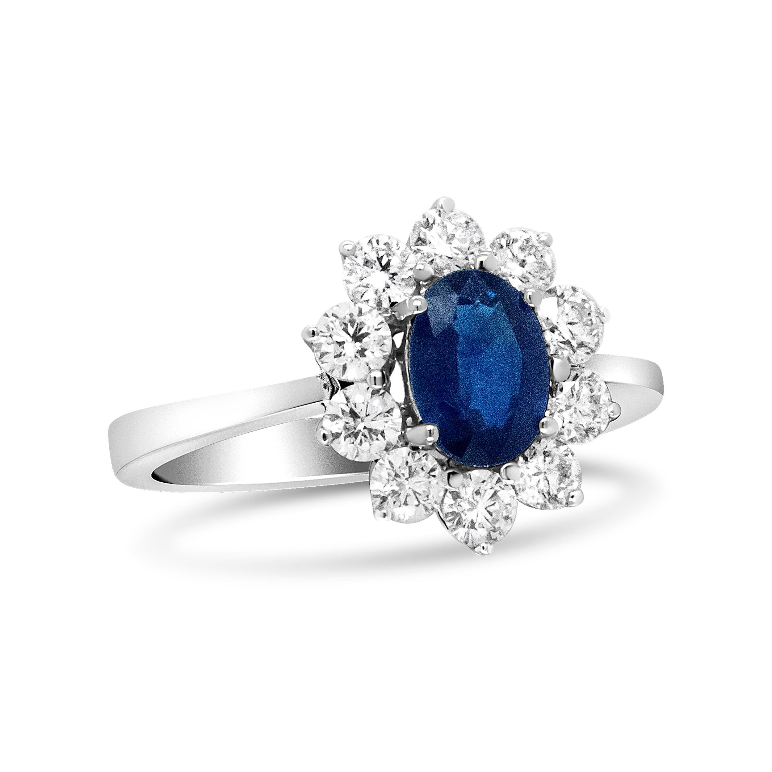 A ring that mirrors that of Diane's, this 18k white gold is beautifully set with a deep blue sapphire gemstone at its center. This 7x5mm stone is flanked by a floral cluster of natural white, round-cut diamonds all along the sides. The total carat