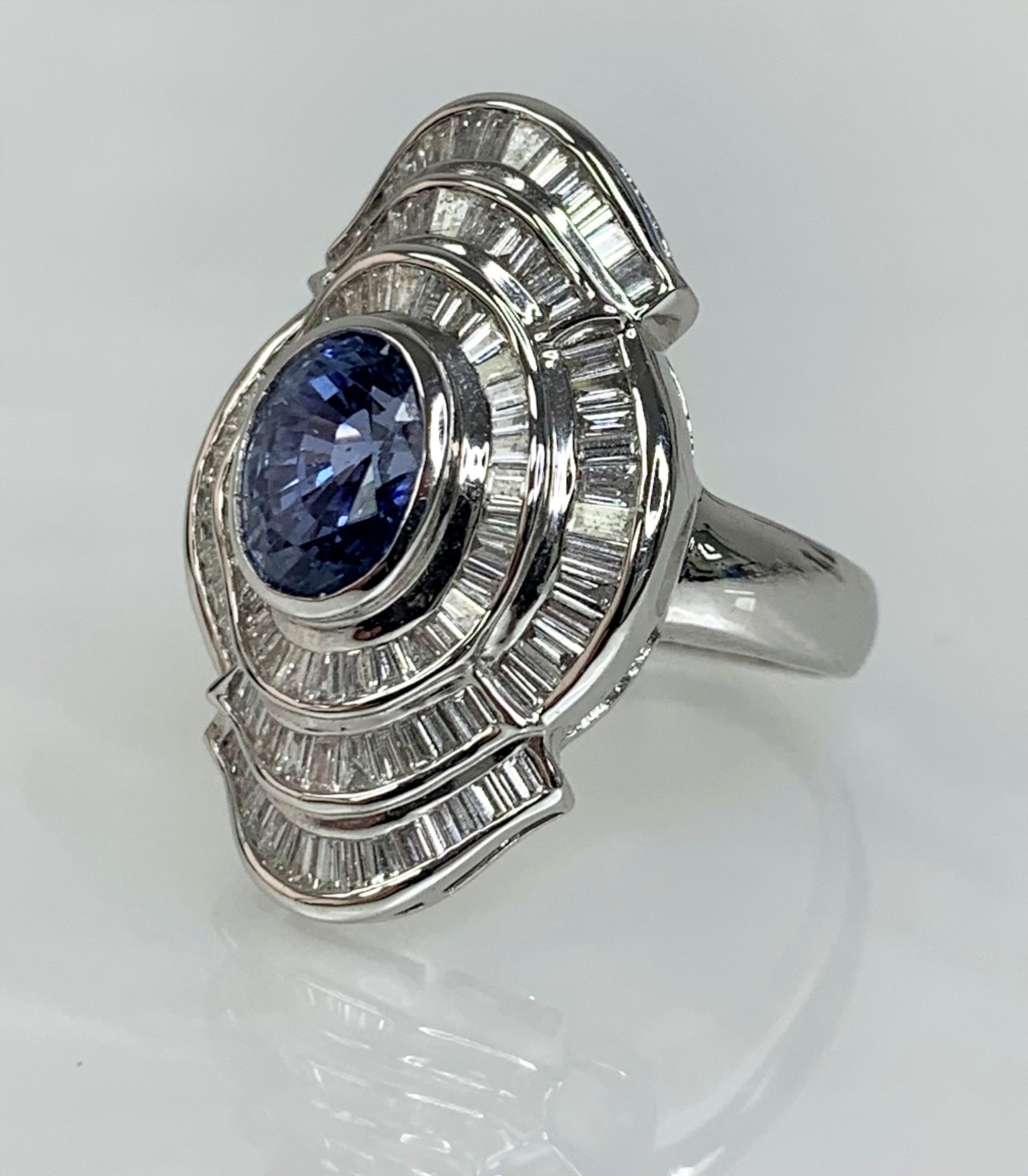 An eye-catching vintage blue sapphire ring featuring a vibrant pastel colored center stone weighing 3.26 carats secured by a bezel setting while uniquely surrounded by 3 rows of sparkling white baguette diamonds weighing 1.85 carats set in solid 18K