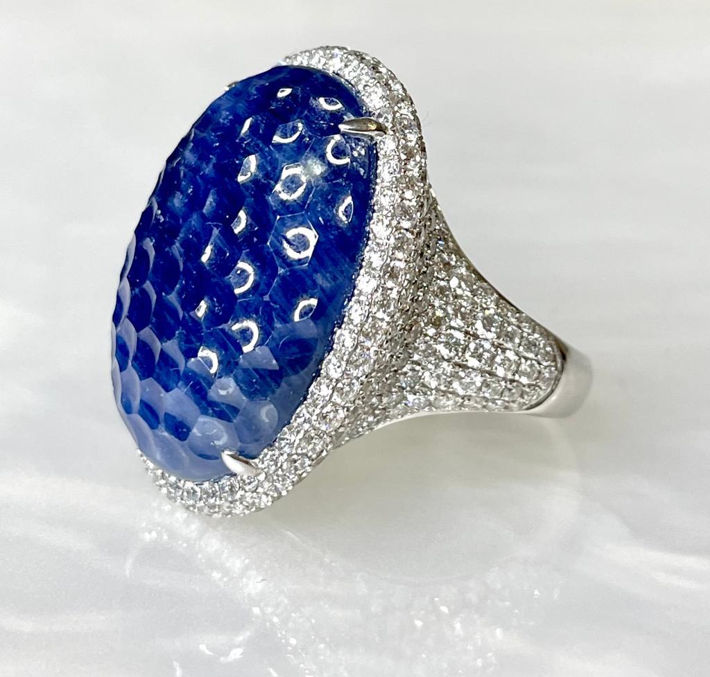 A captivating and luxurious work of art. This natural blue sapphire ring boasts a rare oval shaped center stone weighing 32.33 carats with an unusual “pineapple cut” faceting while surrounded by 5.49 carats of sparkling white diamonds set in solid